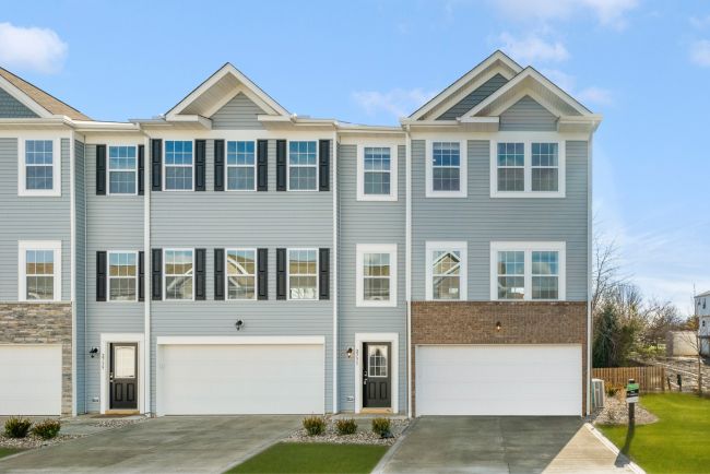 Modern townhome exterior featuring a blue facade, multiple windows, and two garage doors.