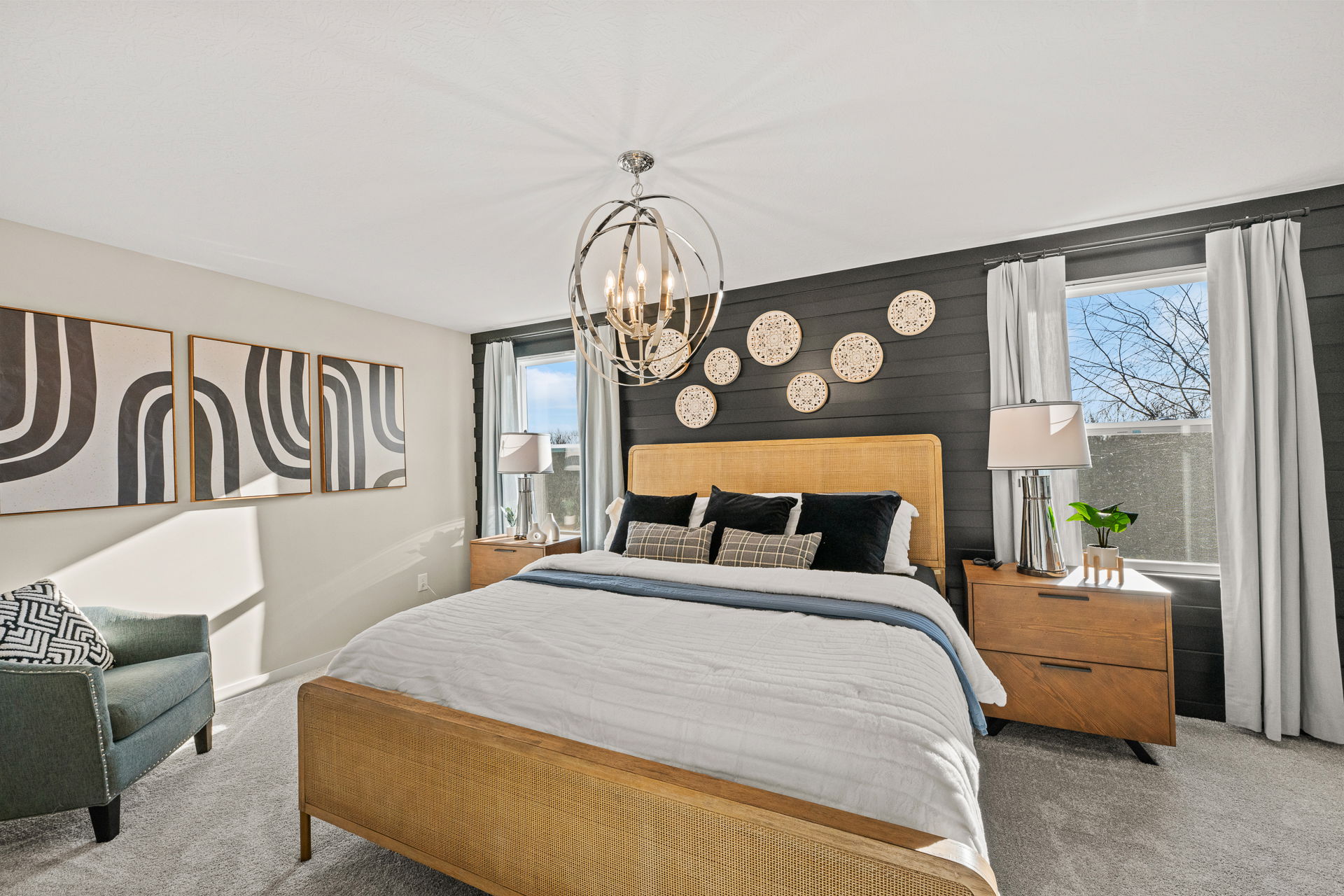 A stylish modern bedroom featuring a rattan bed, decorative wall plates, and a cozy seating area with natural light streaming through the windows.