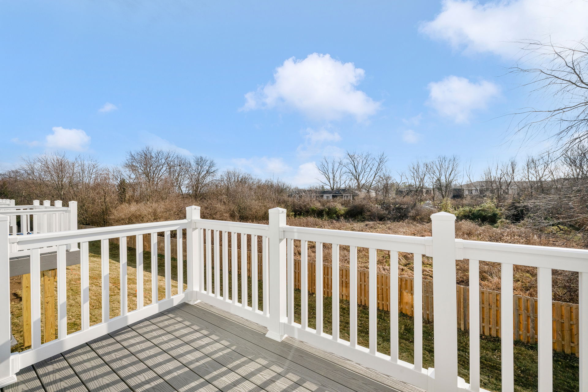 View from a balcony with a white railing overlooking a grassy area and trees under a clear blue sky.