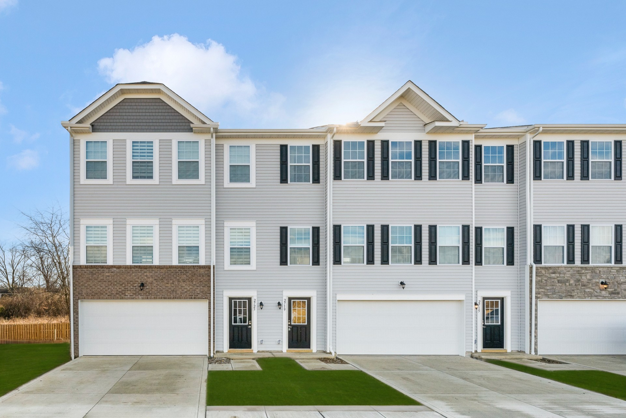 Modern townhouses with brick accents and manicured lawns under a clear blue sky.