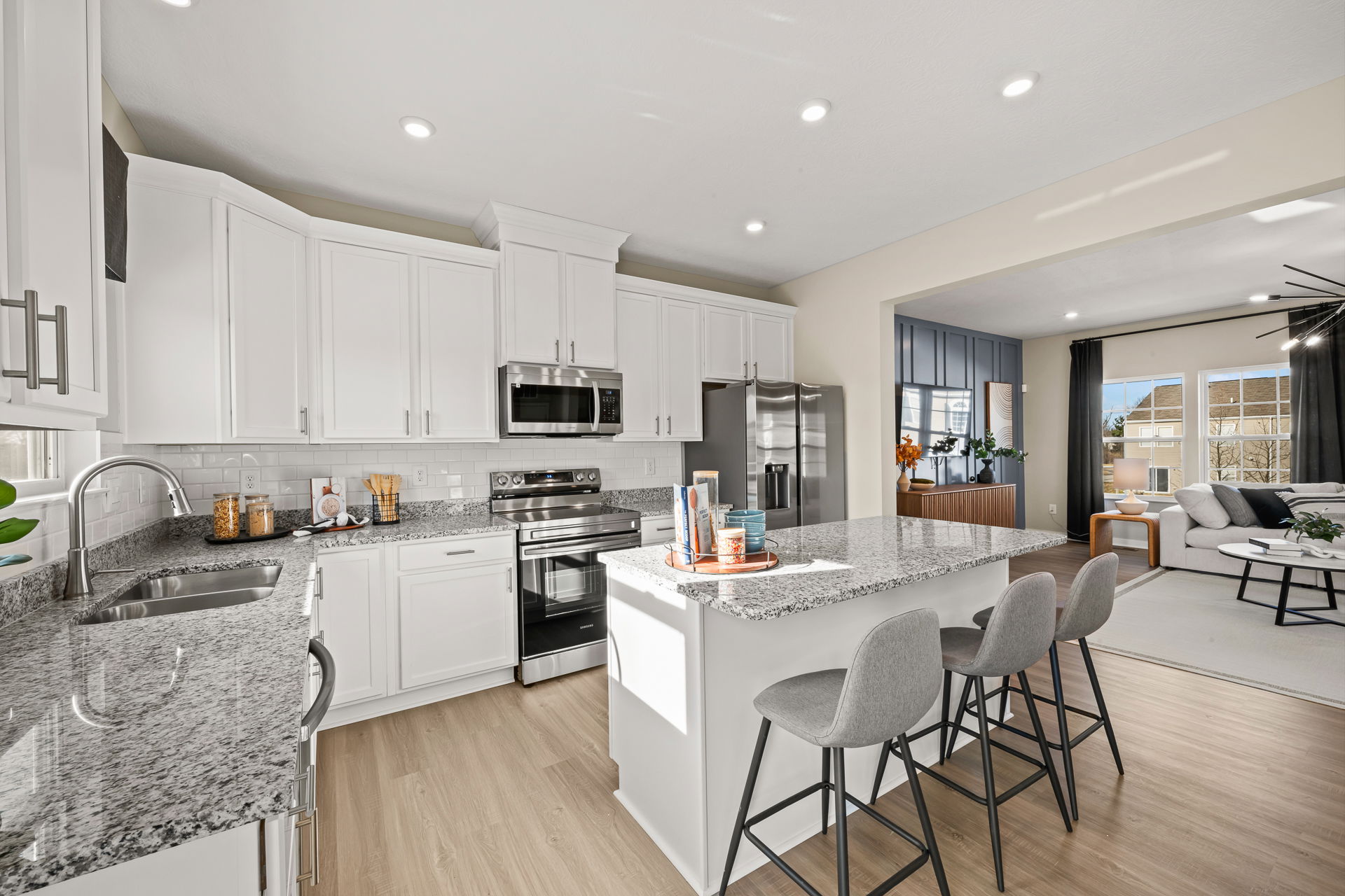 Modern kitchen featuring white cabinets, granite countertops, stainless steel appliances, and stylish seating.