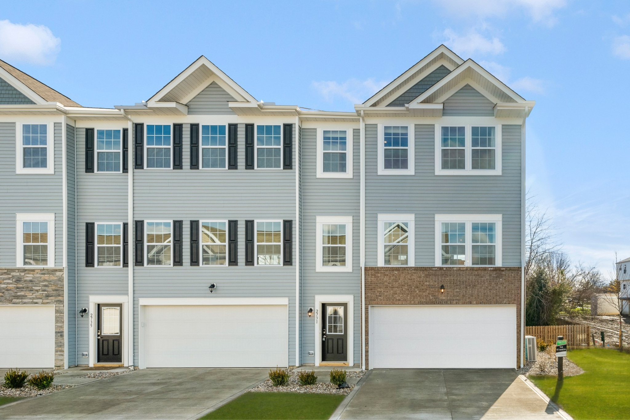Modern two-story townhouse with a stone and siding exterior, featuring large windows and double garage doors.