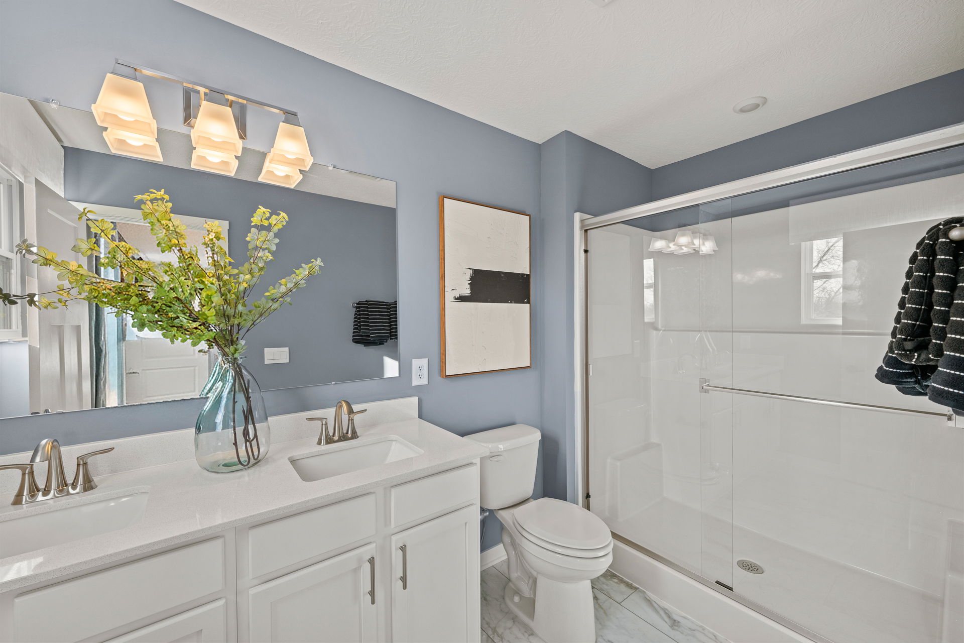 Modern bathroom interior featuring a double vanity, stylish light fixtures, and a glass shower enclosure with decorative elements.