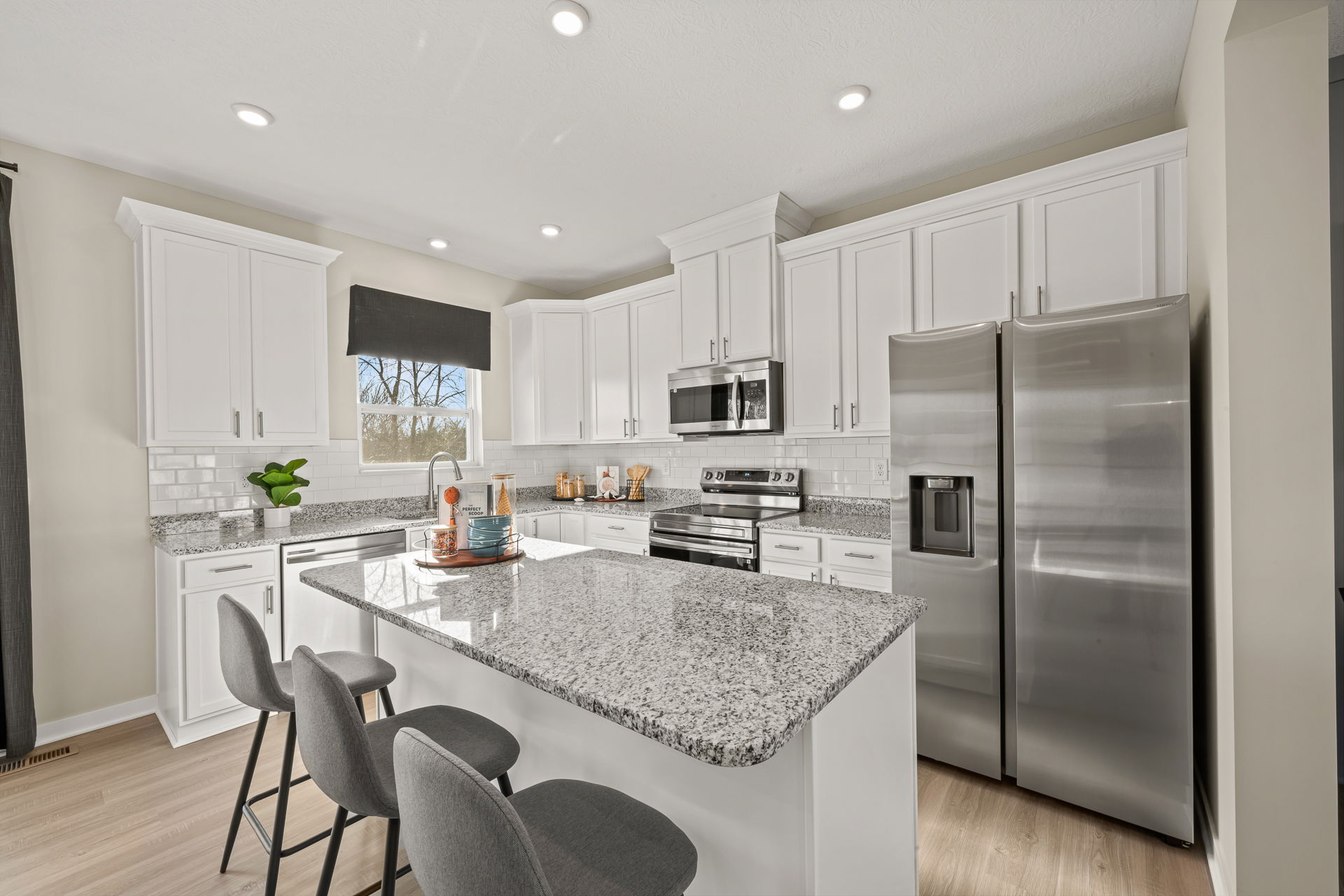 Modern kitchen interior featuring white cabinets, granite countertops, stainless steel appliances, and contemporary bar seating.