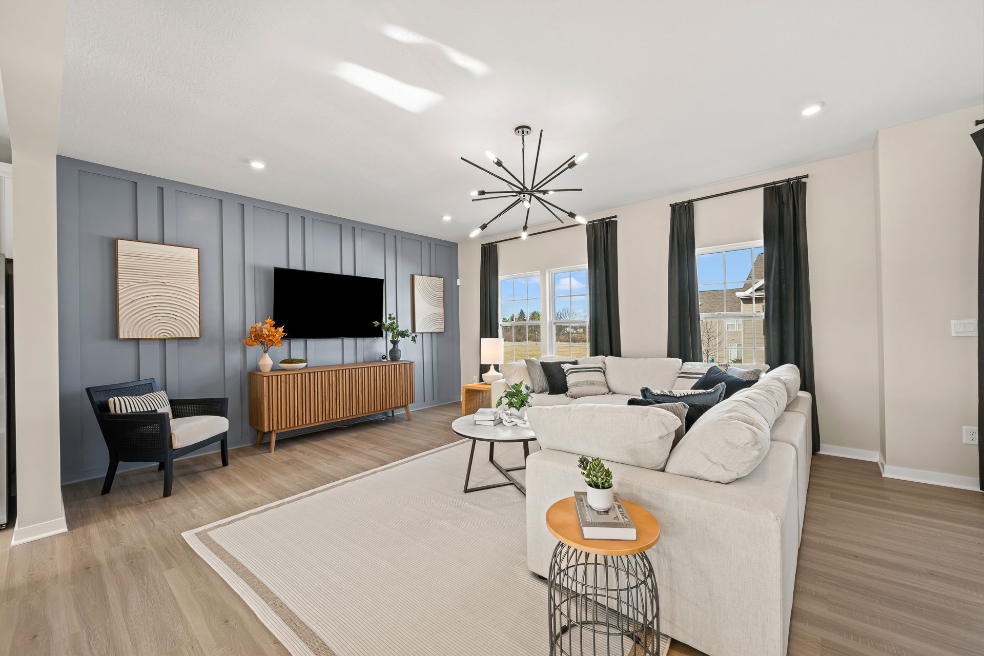 Modern living room featuring a cozy sectional sofa, decorative wall art, stylish lighting, and large windows with natural light.