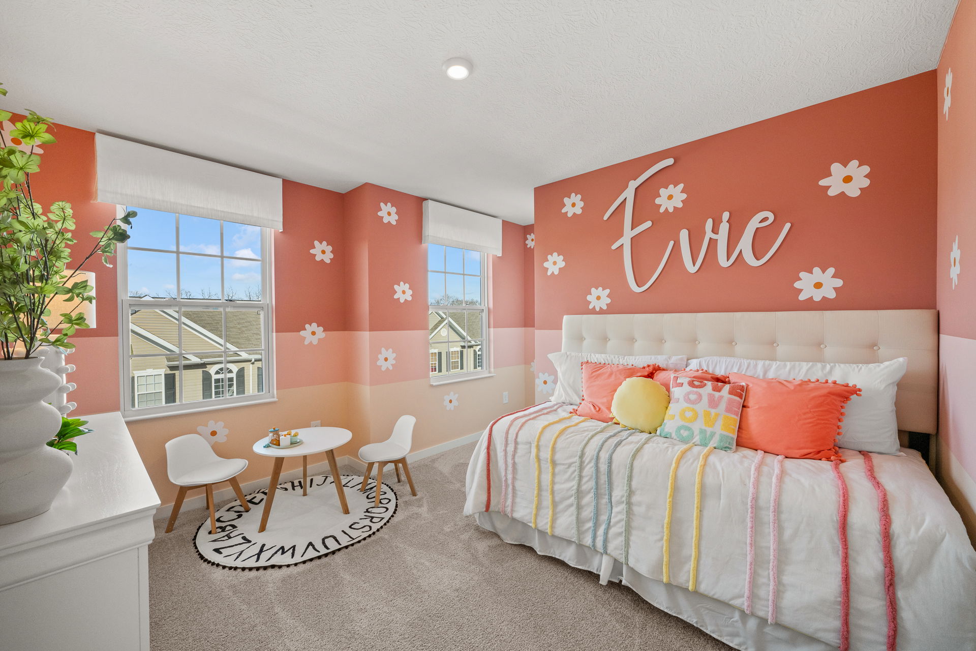 Bright and colorful children's bedroom featuring a pink flower-themed wall, cozy bedding, and a playful seating area with a round rug.