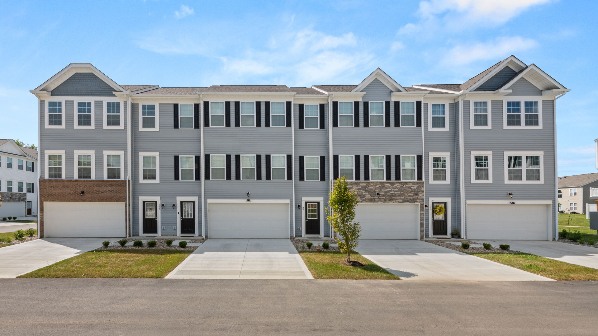 Modern multi-family townhomes with spacious garages and vibrant landscaping in a suburban setting.