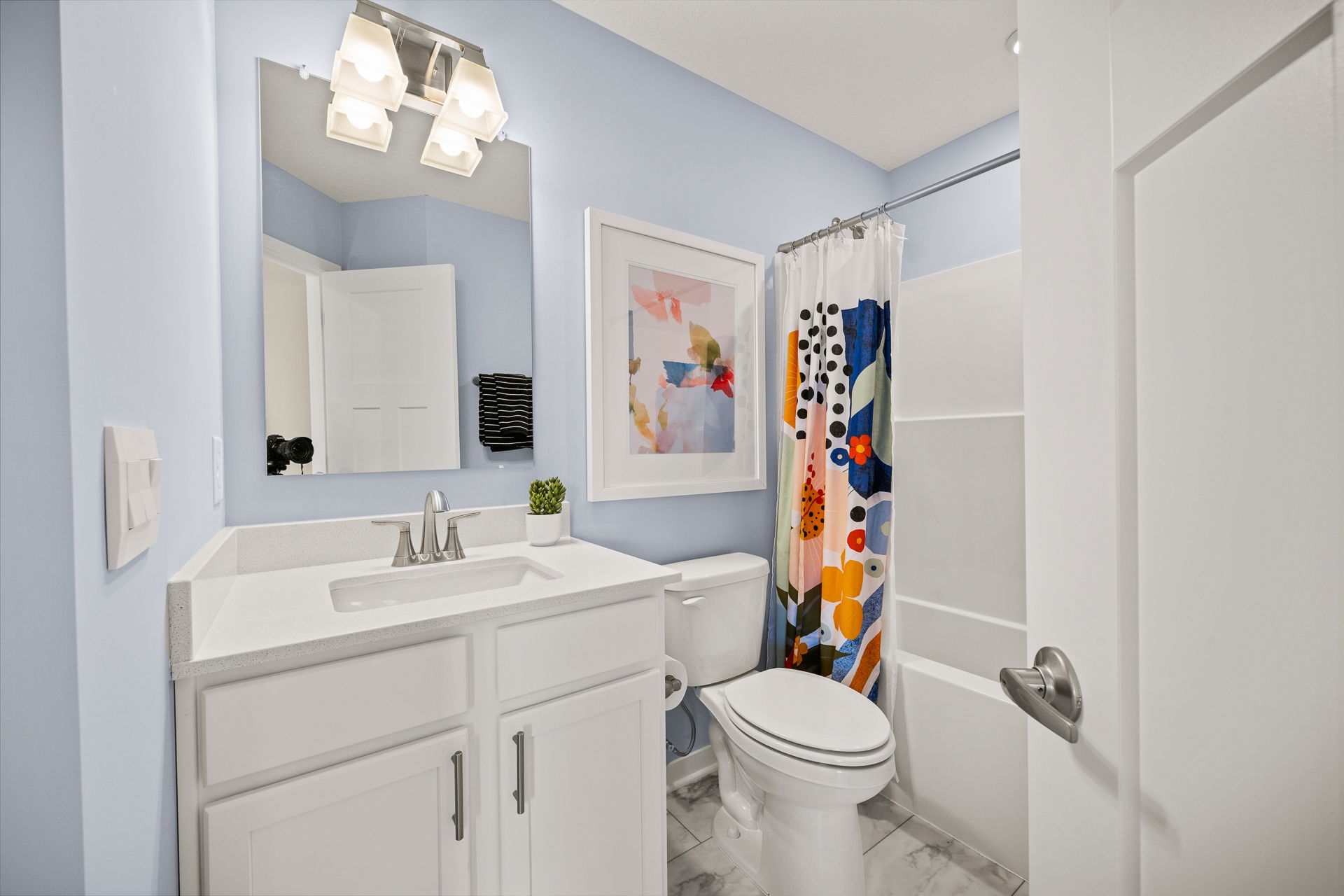 A bright and modern bathroom featuring a white vanity, colorful shower curtain, and light blue walls.