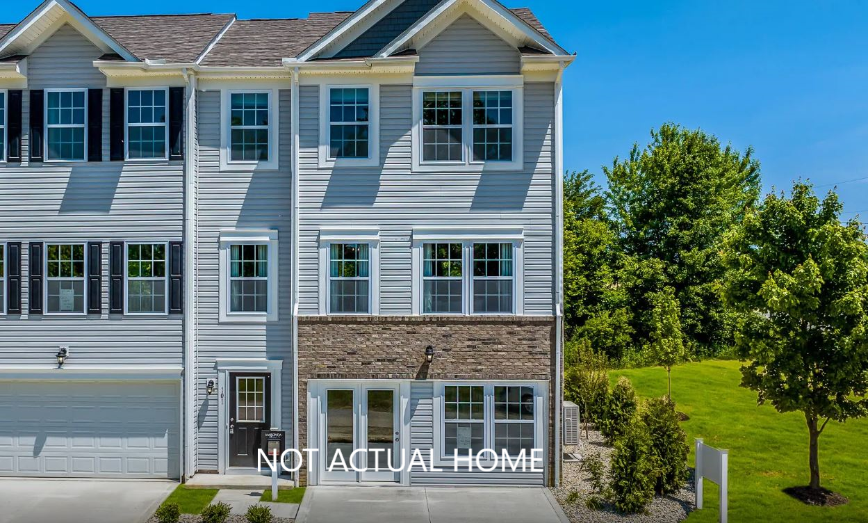 Modern multi-story townhouse with a brick and siding exterior set against a backdrop of green trees and a clear blue sky, labeled 