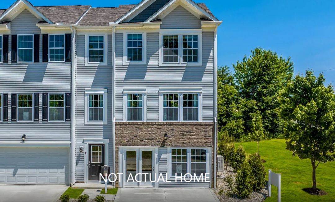 Modern townhouse exterior with gray siding and multiple windows, surrounded by greenery under a clear blue sky.