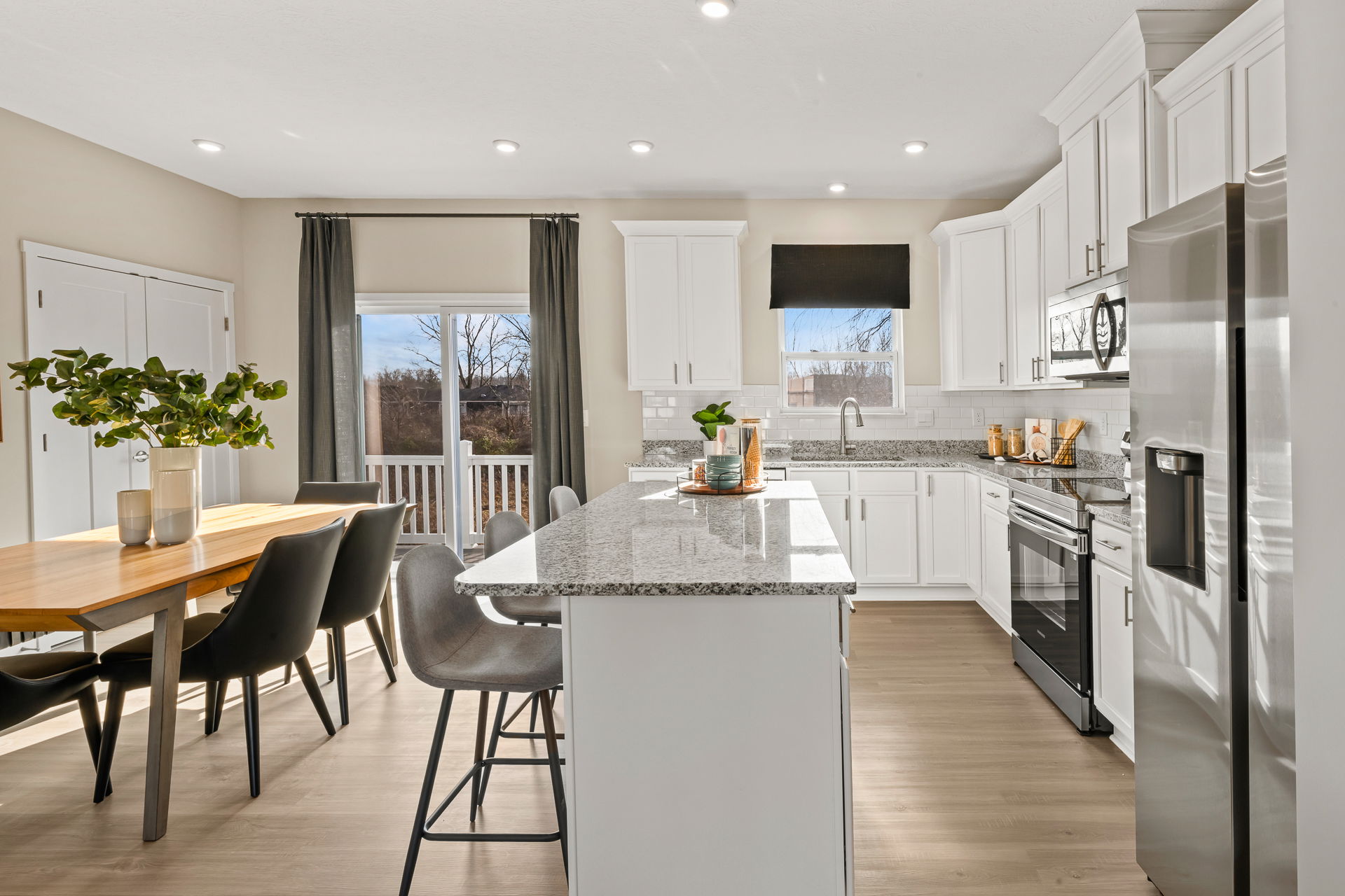 Modern kitchen interior featuring white cabinets, granite countertops, a dining area with a wooden table, and natural light from large windows.