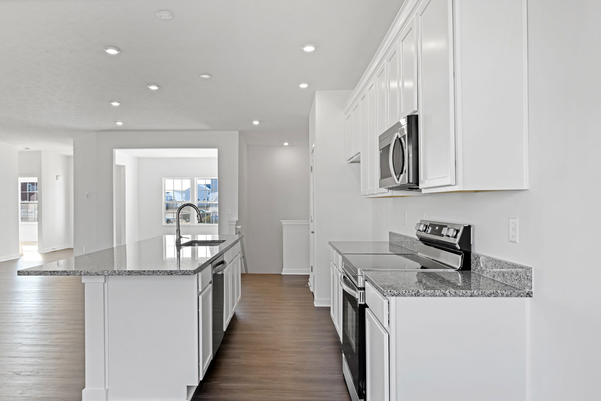 Modern kitchen with granite countertops, white cabinets, stainless steel appliances, and hardwood flooring.