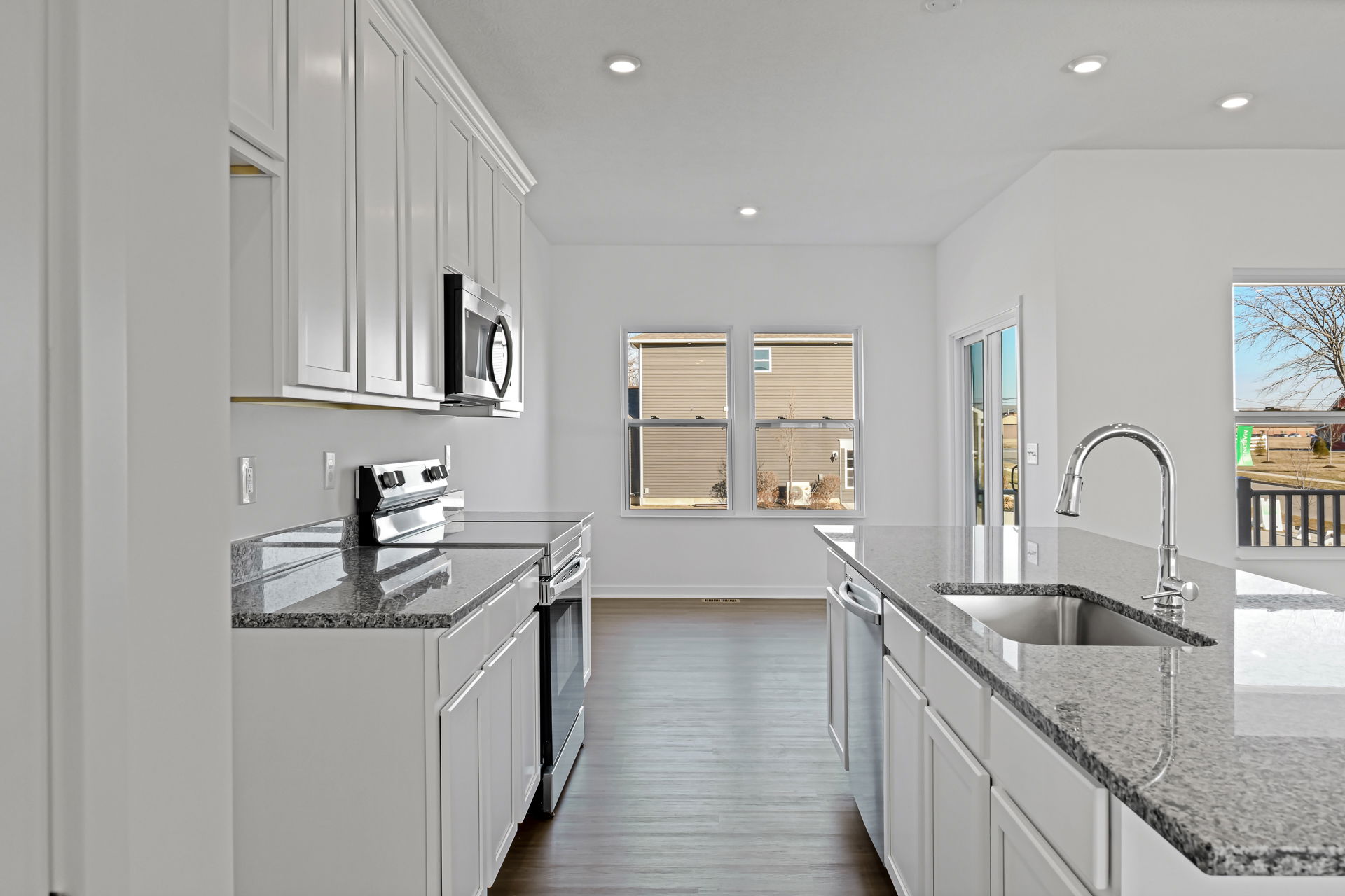 Modern kitchen interior with white cabinets, granite countertops, stainless steel appliances, and hardwood flooring.
