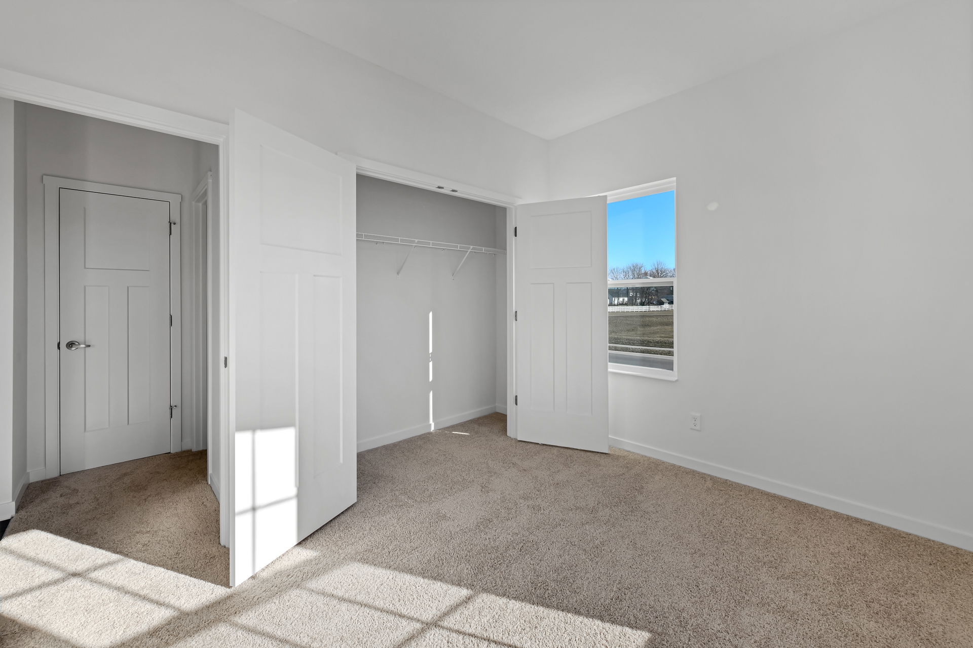 Empty room with beige carpet, open closet doors, and a window letting in natural light.