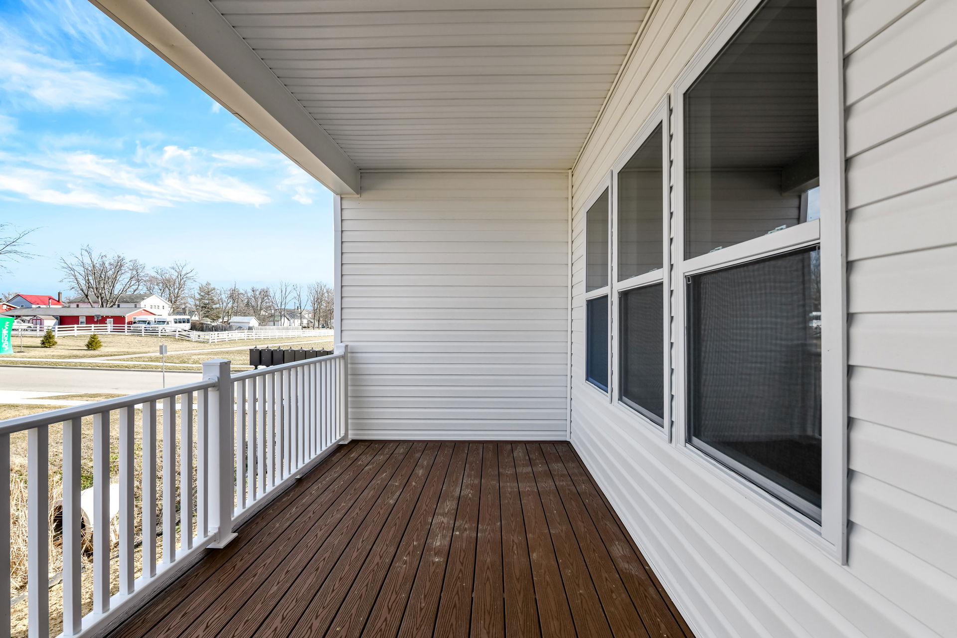 A wooden porch with white railing attached to a white-paneled house, overlooking a suburban neighborhood.