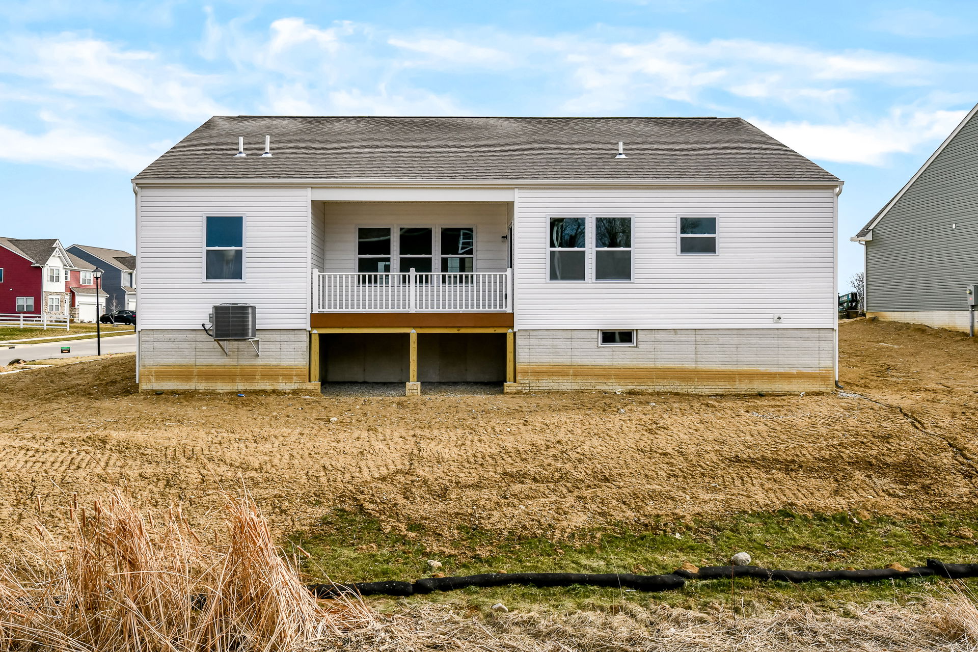 Rear view of a newly constructed white house with a covered porch and adjacent suburban homes.