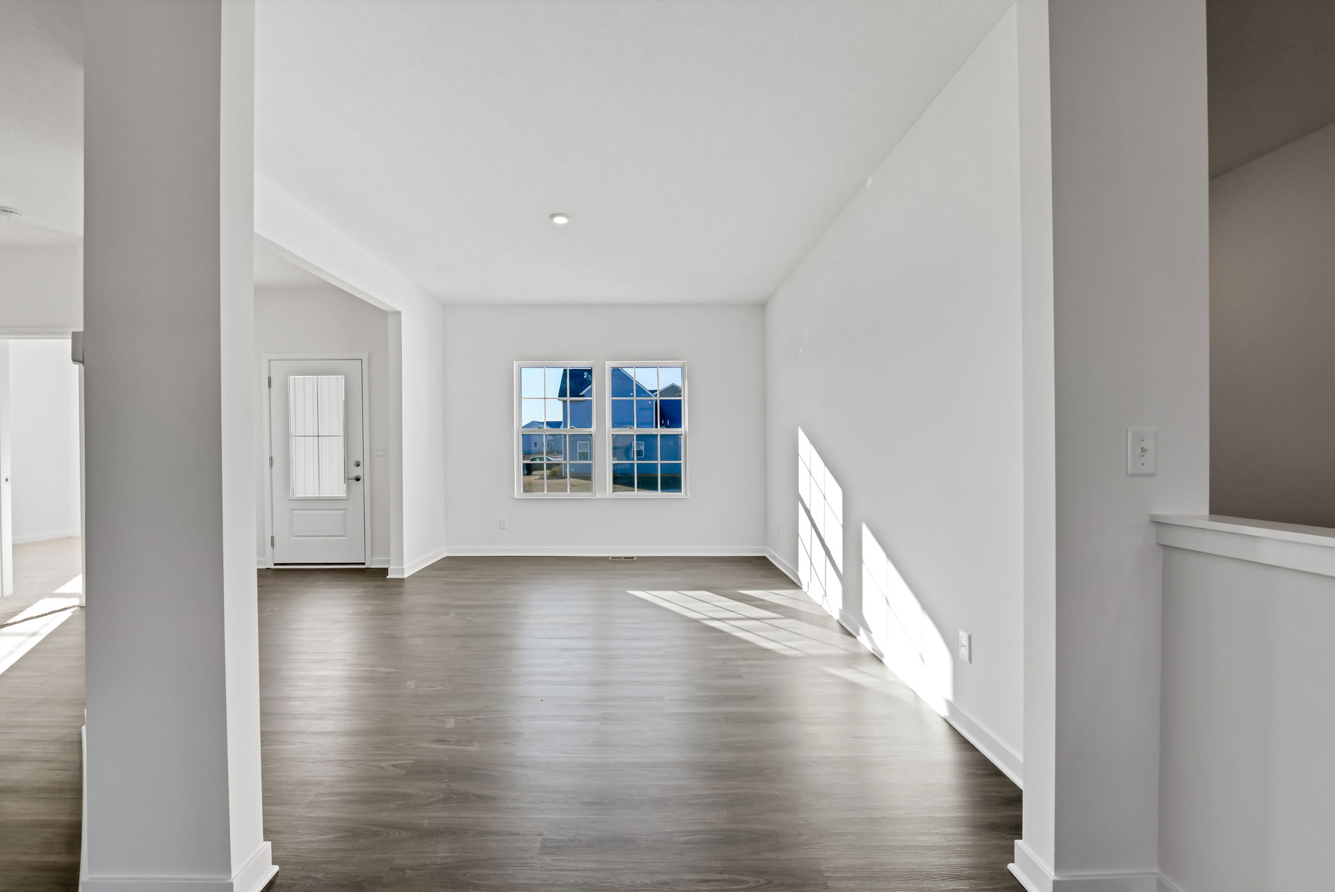Spacious empty room with large windows, wood flooring, and white walls, highlighting natural light.