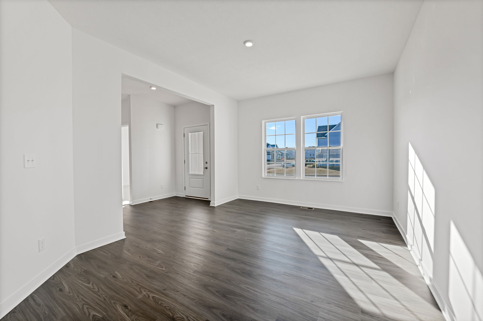 Bright, empty room with white walls, large windows, and dark wood flooring showcasing a modern interior design.