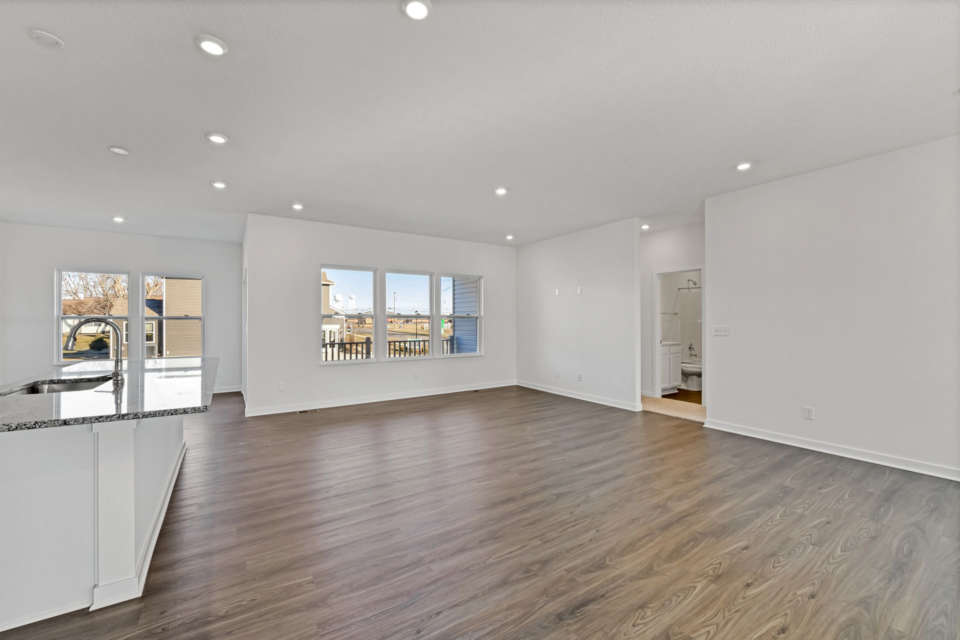 Spacious, modern open-concept living room with hardwood floors, white walls, and large windows offering natural light.