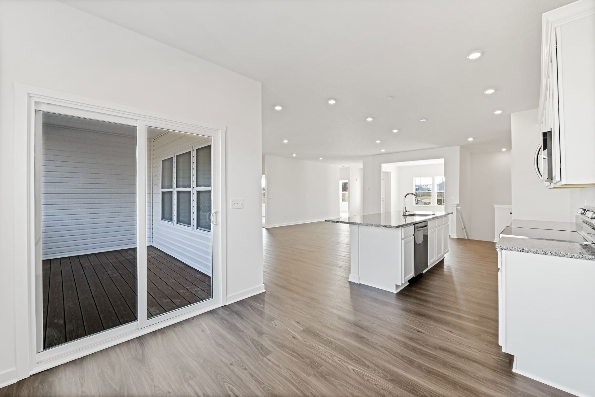 Spacious modern kitchen with granite countertops, hardwood floors, and large sliding doors leading to a decked patio.