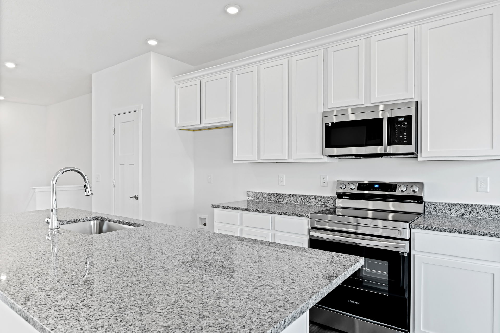 Modern kitchen with granite countertops, stainless steel appliances, and white cabinetry.