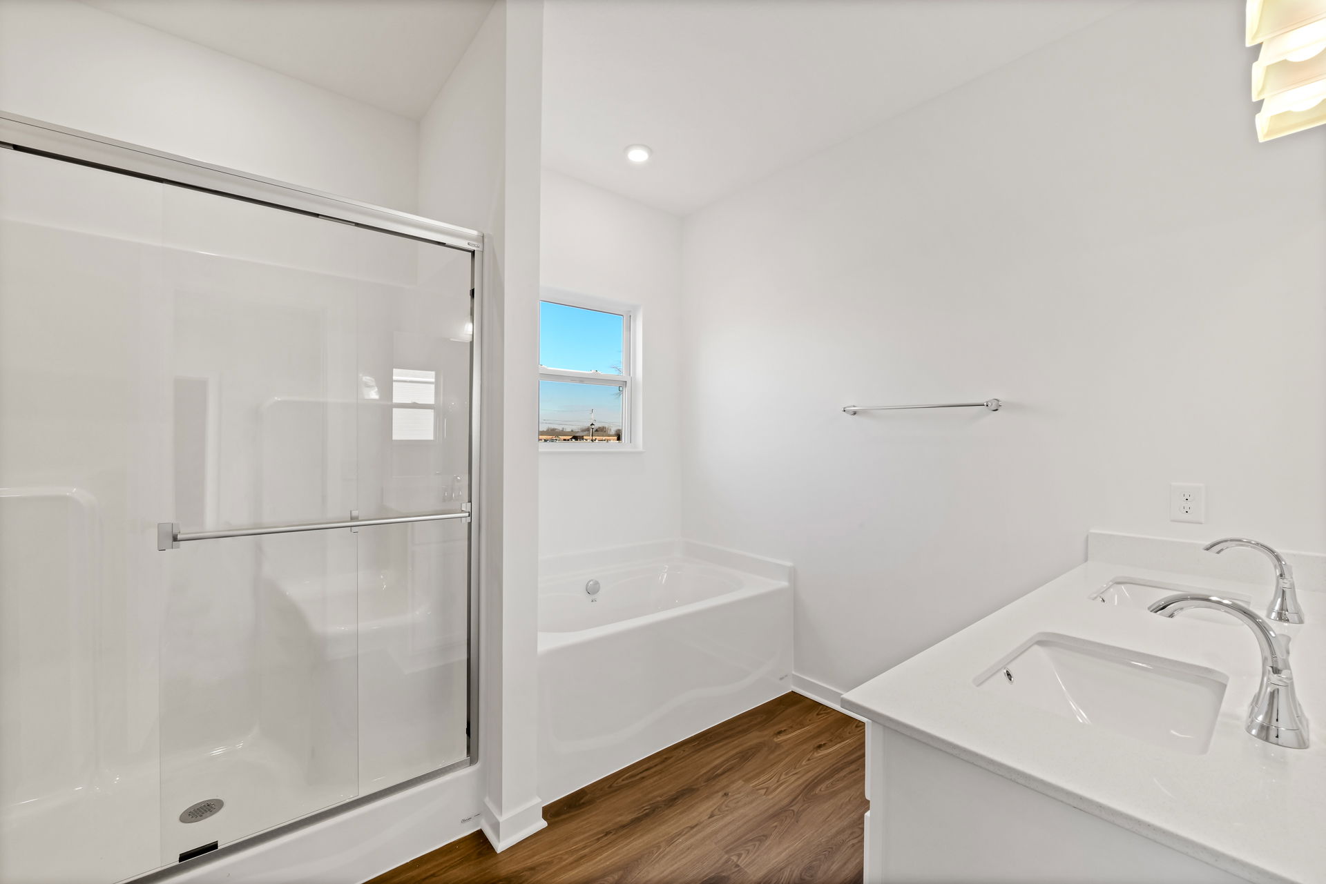 Modern bathroom with a glass shower, white bathtub, dual sink vanity, and wood flooring.