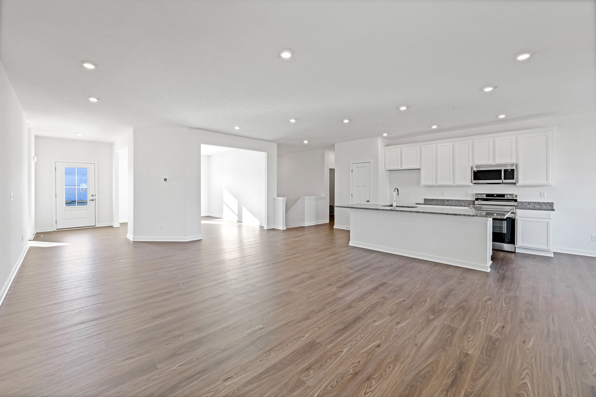 Spacious modern kitchen and living area with hardwood floors and white cabinetry.