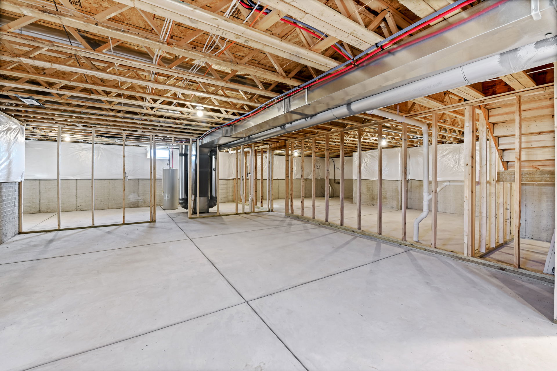Spacious unfinished basement with exposed wood framing, ductwork, and concrete floor, ideal for renovation or remodeling projects.