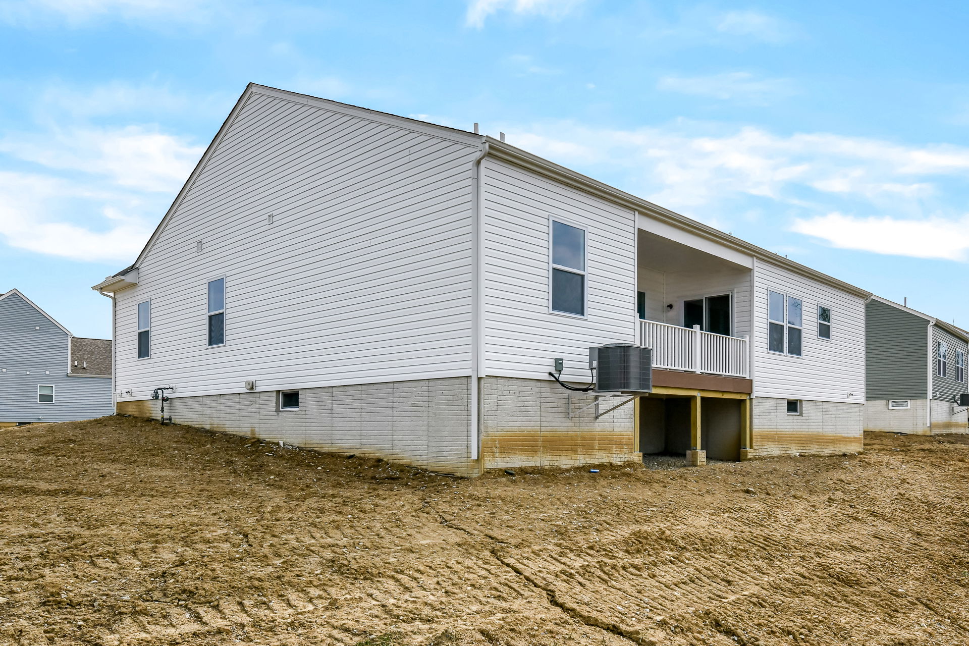 Exterior view of a newly constructed single-story house with white siding, a sloped yard, and an elevated deck area.