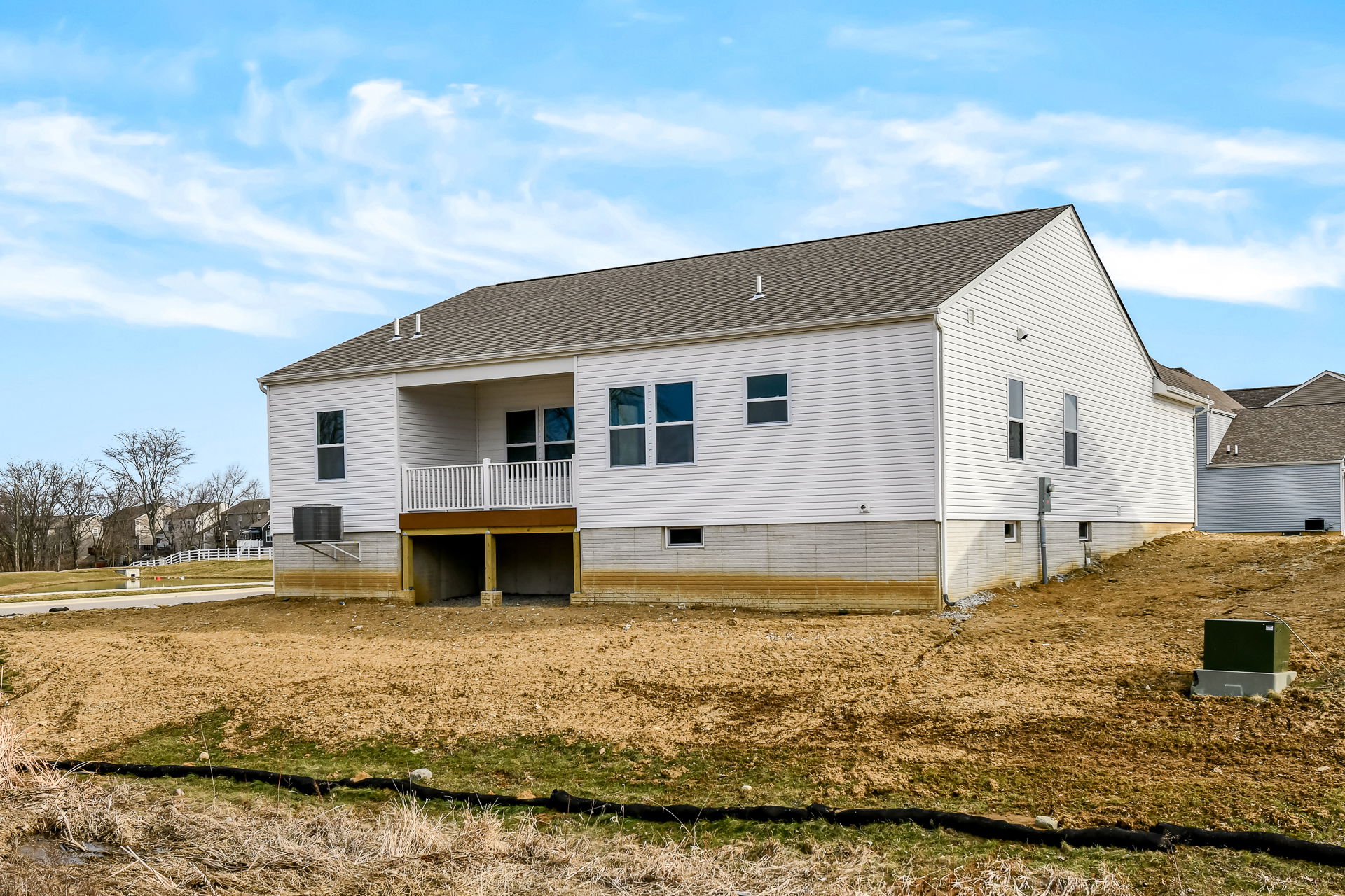 Newly constructed white house with a spacious back porch and unfinished yard under a clear blue sky.