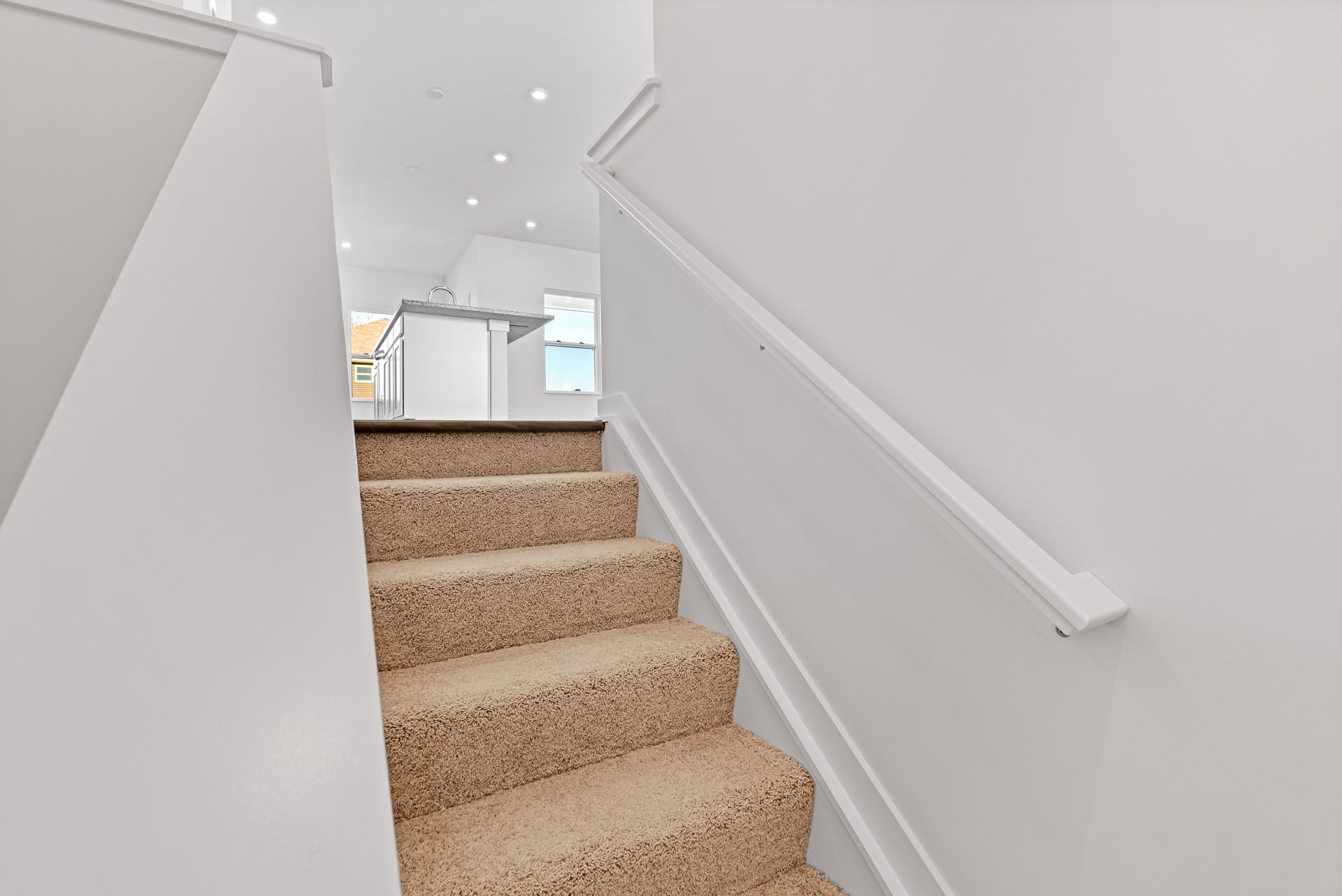 Carpeted stairs leading up to a modern kitchen with bright lighting and white cabinets.