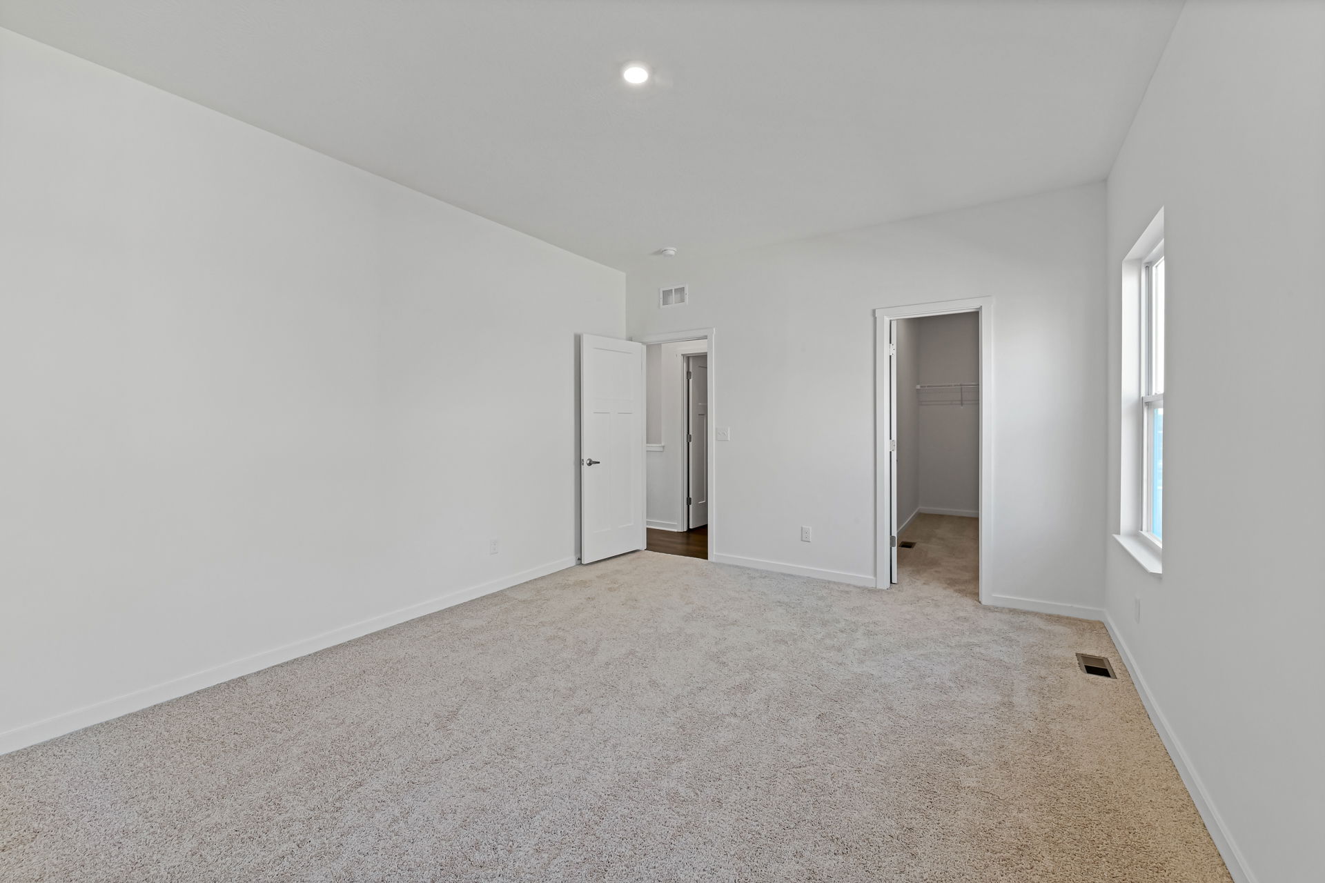 Spacious, empty bedroom with white walls, beige carpet, and a walk-in closet door.