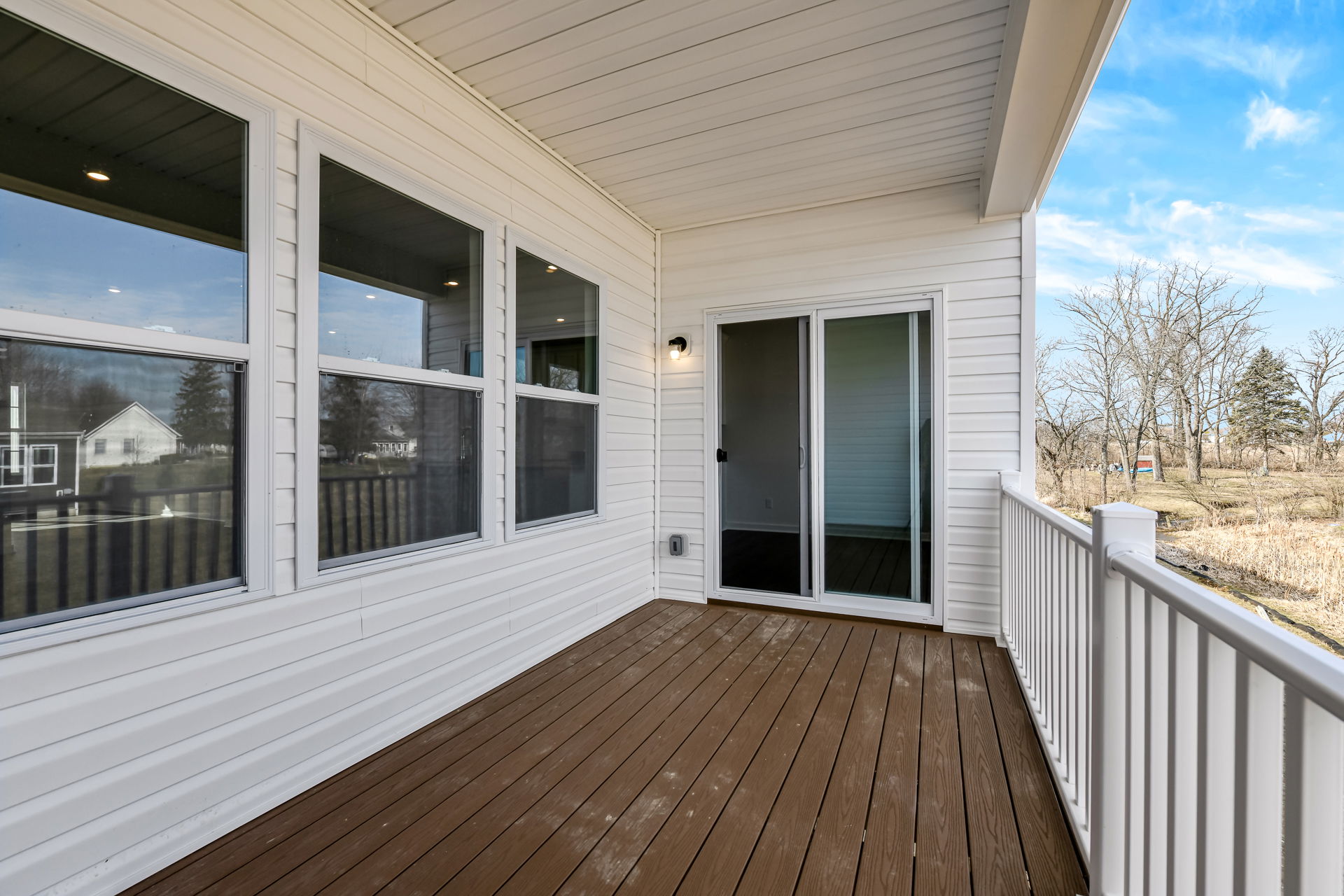 Covered porch with sliding glass door and wooden deck overlooking a scenic backyard with trees.