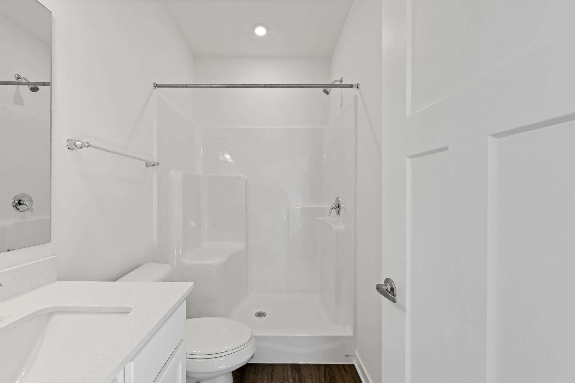 Modern white bathroom featuring a walk-in shower, toilet, and vanity with wood flooring.