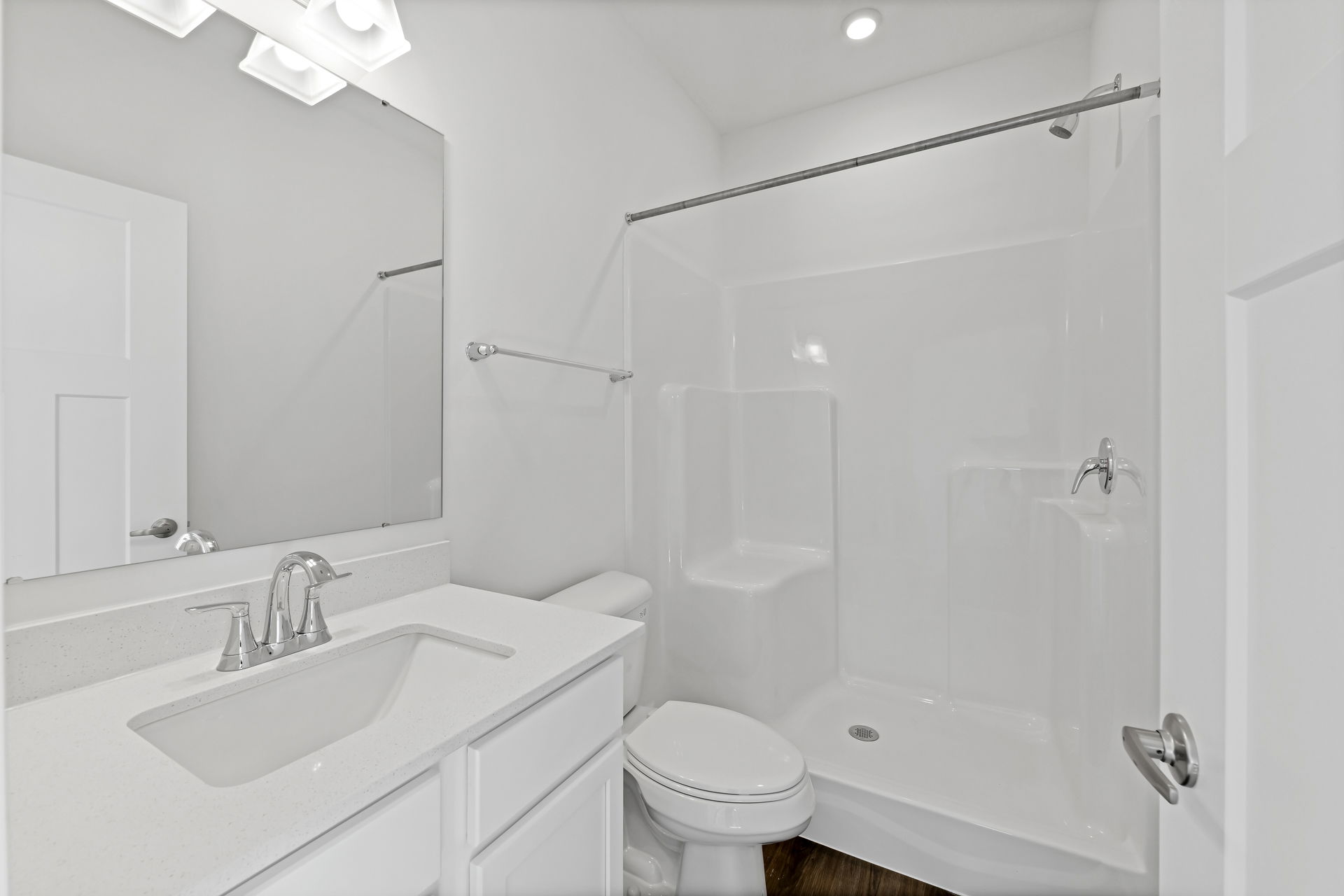 Modern white bathroom featuring a sleek vanity, large mirror, toilet, and spacious shower enclosure.