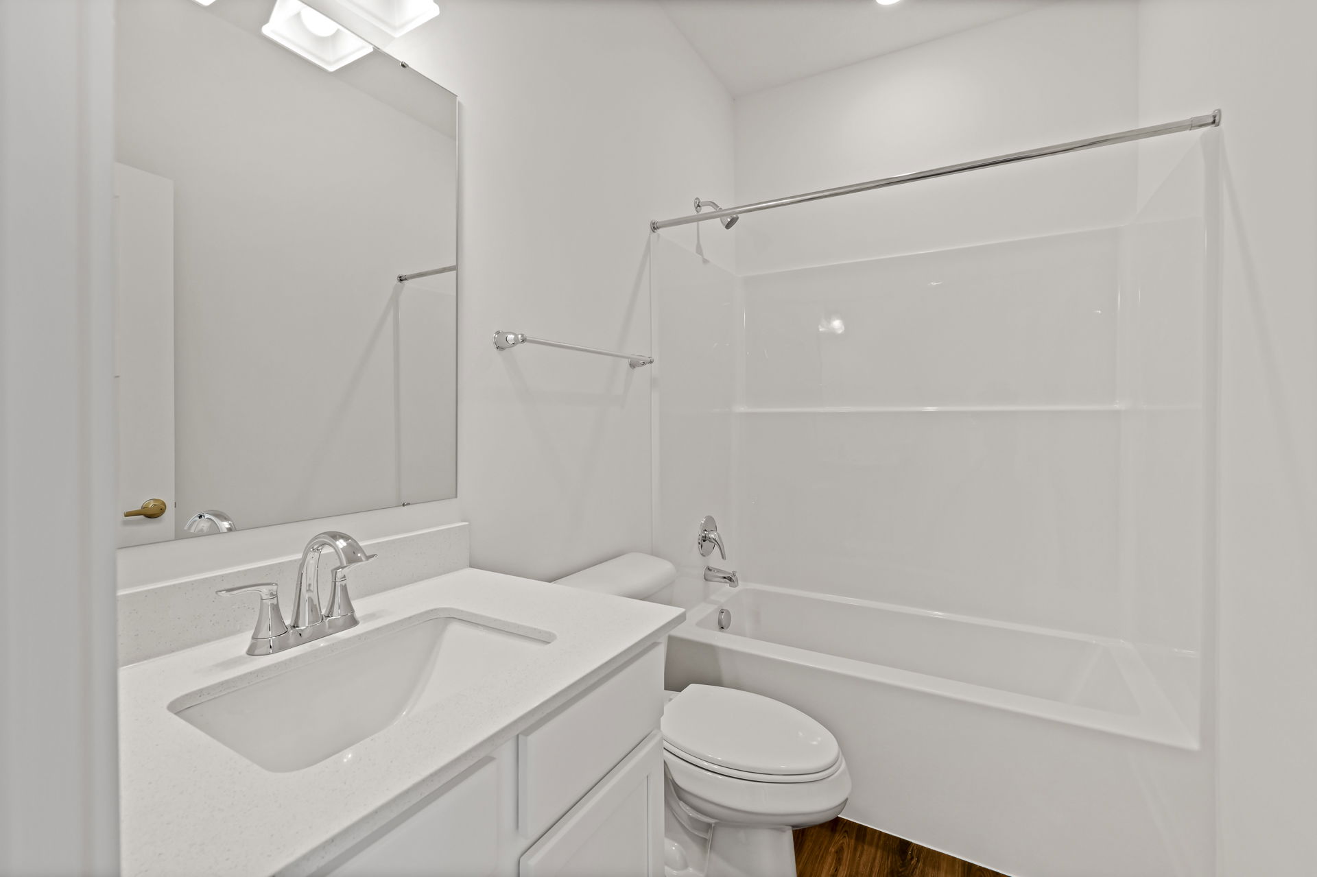 Modern white bathroom with vanity sink, large mirror, bathtub, and toilet on a wooden floor.