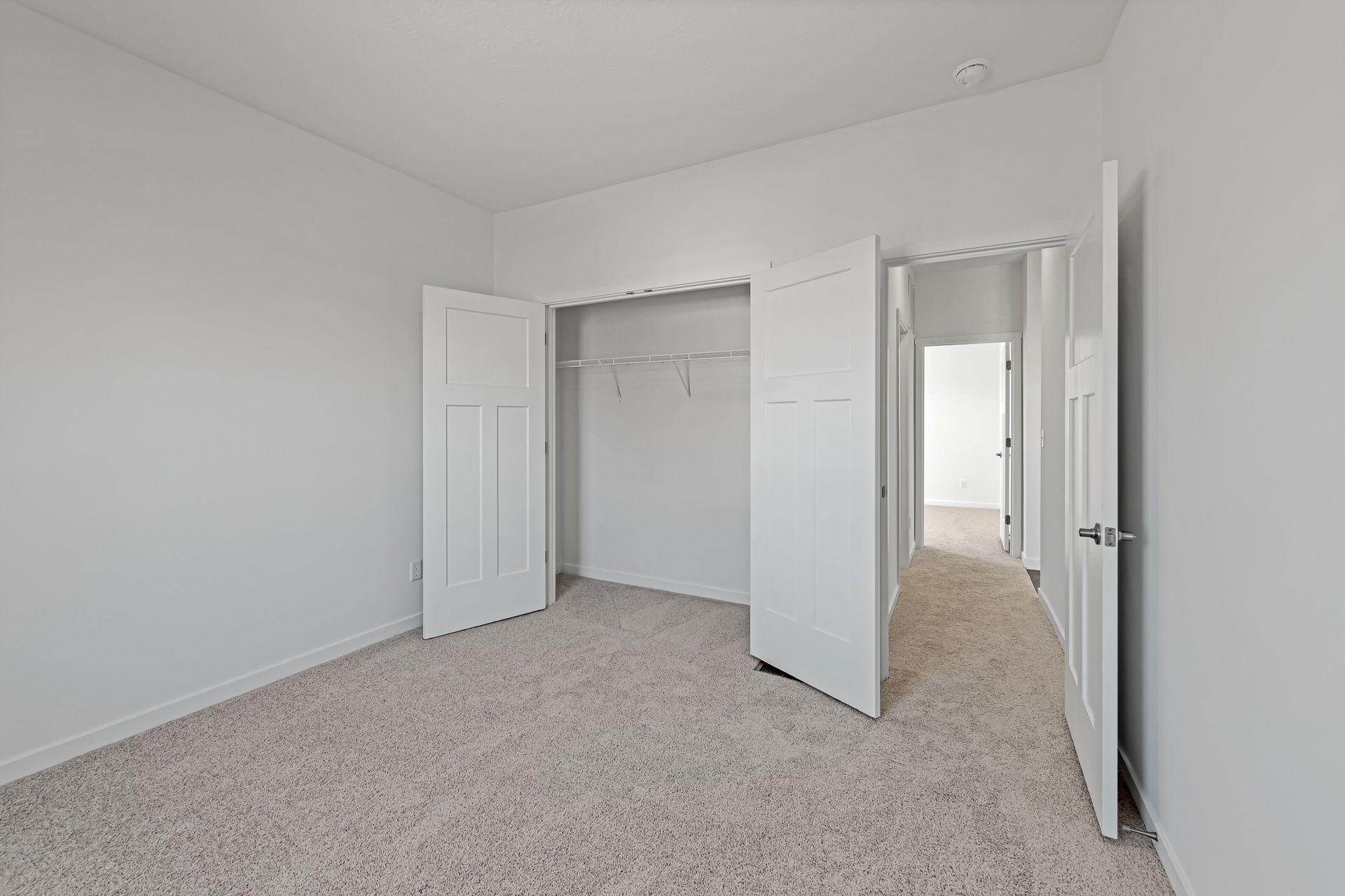 Empty bedroom with open closet doors, beige carpet, and white walls in a modern home.