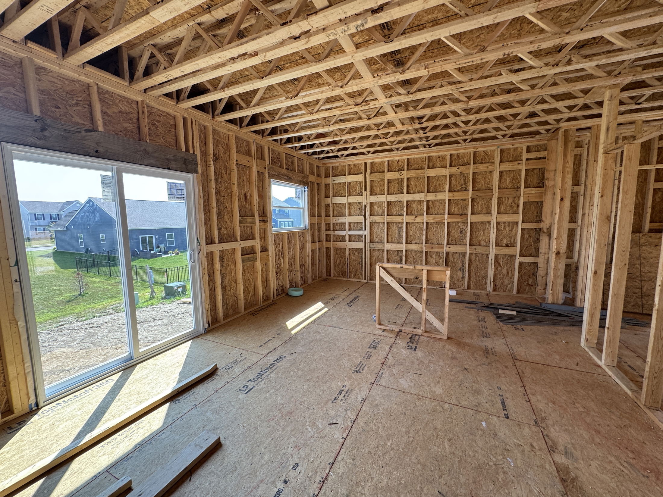 Partially constructed room with wooden framing and exposed trusses, featuring a sliding glass door and outside view of houses.