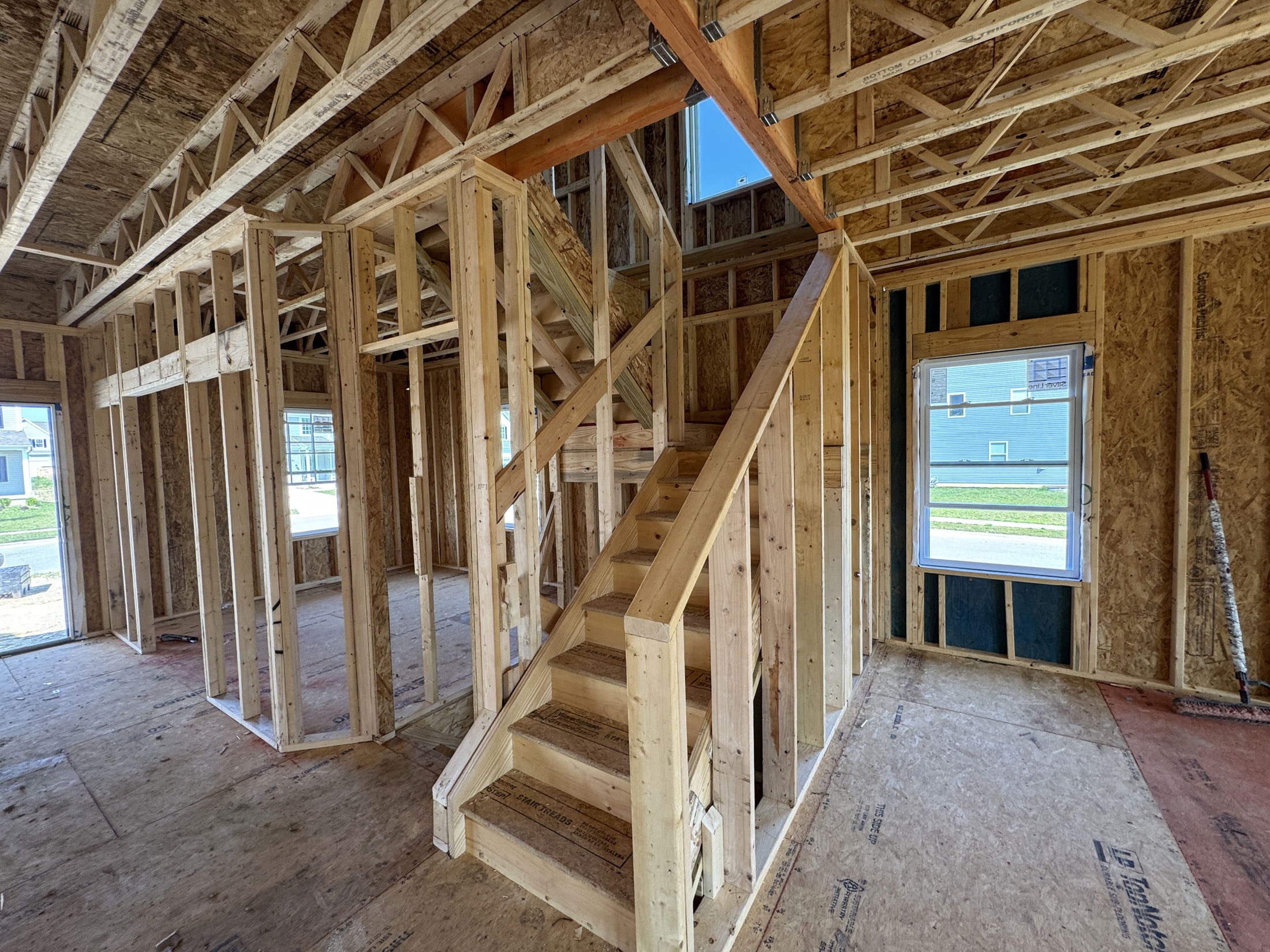 Framed interior of a new house under construction showcasing wooden beams, unfinished walls, and a staircase.