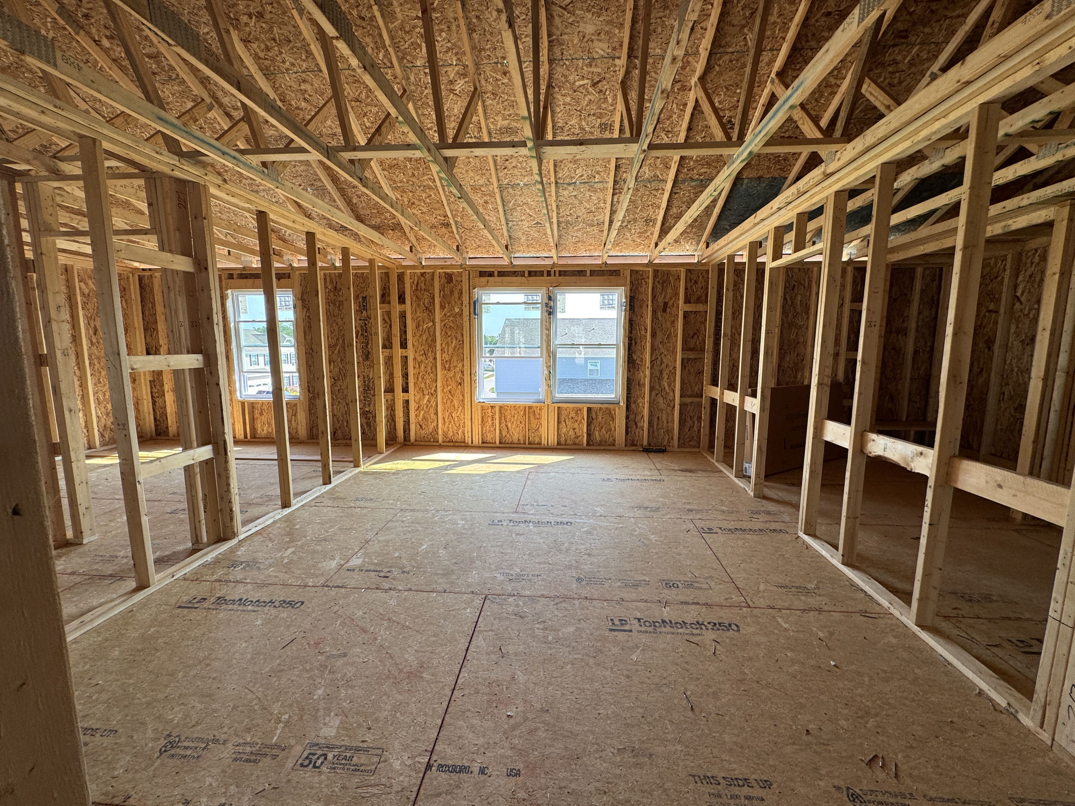 Framed interior of a house under construction showing wooden beams and plywood flooring.
