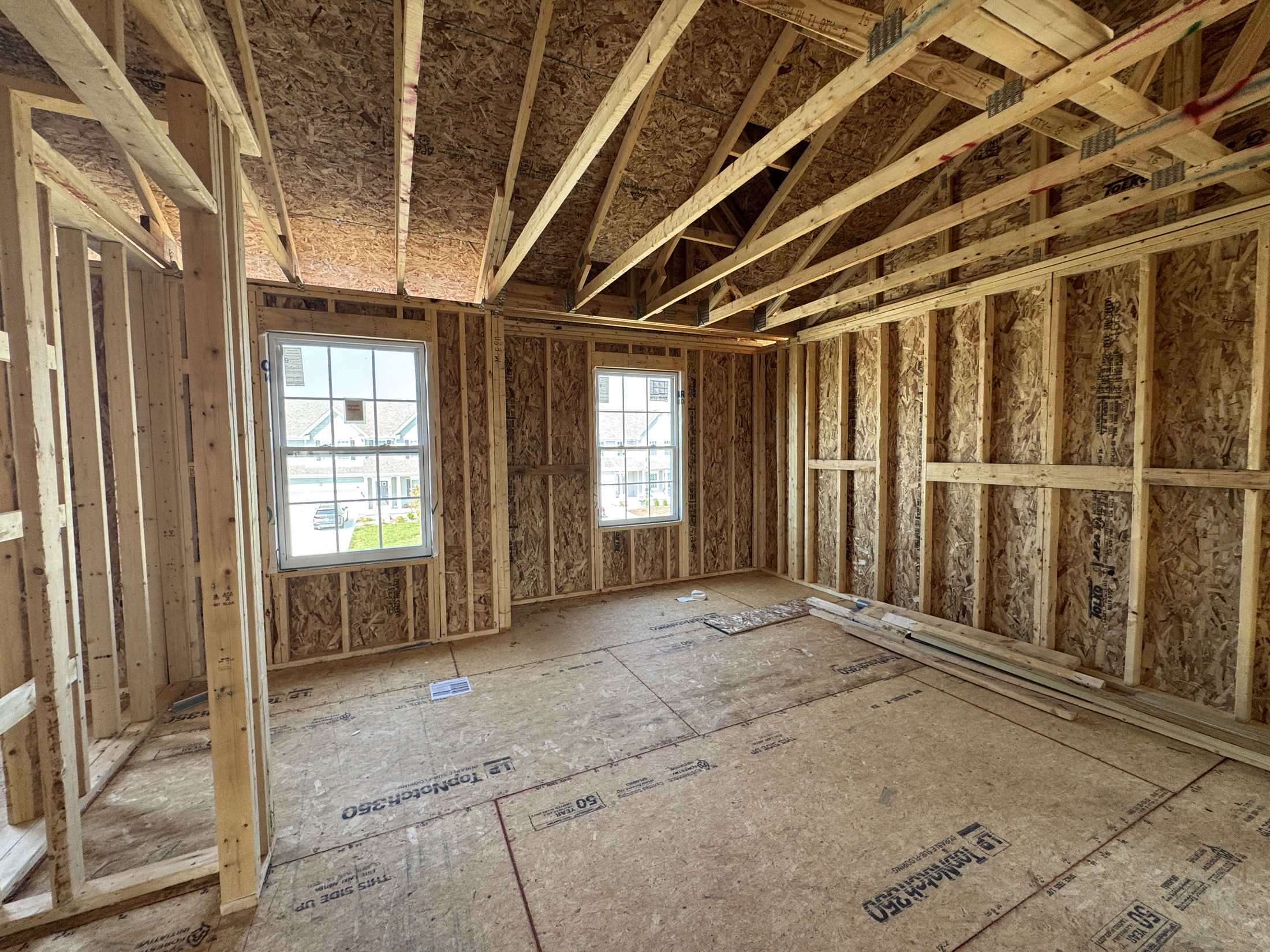 Framed interior of a house under construction, showcasing exposed wooden beams, OSB walls, and two windows.