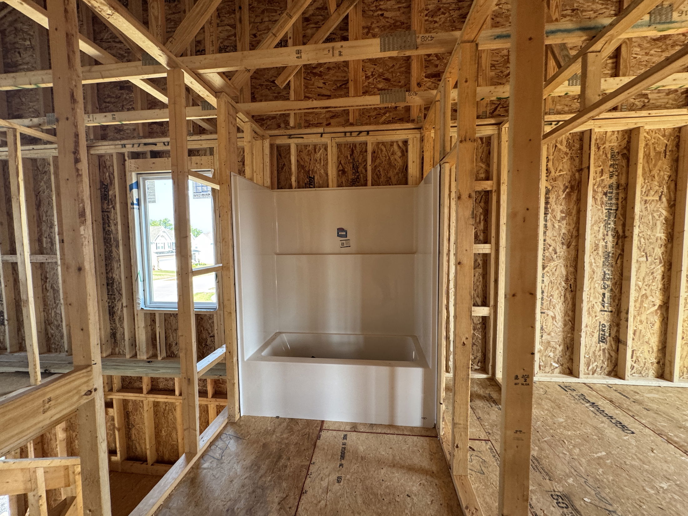 Partially constructed house with exposed wooden framing and an installed bathtub.