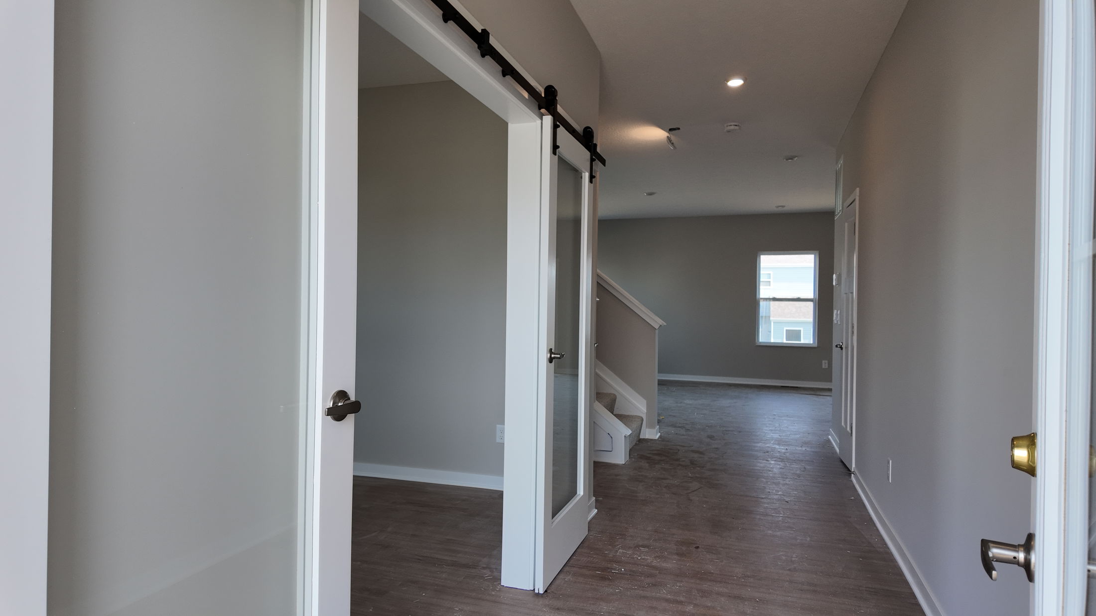 Modern home interior showcasing a hallway with sliding glass barn doors and wood flooring.