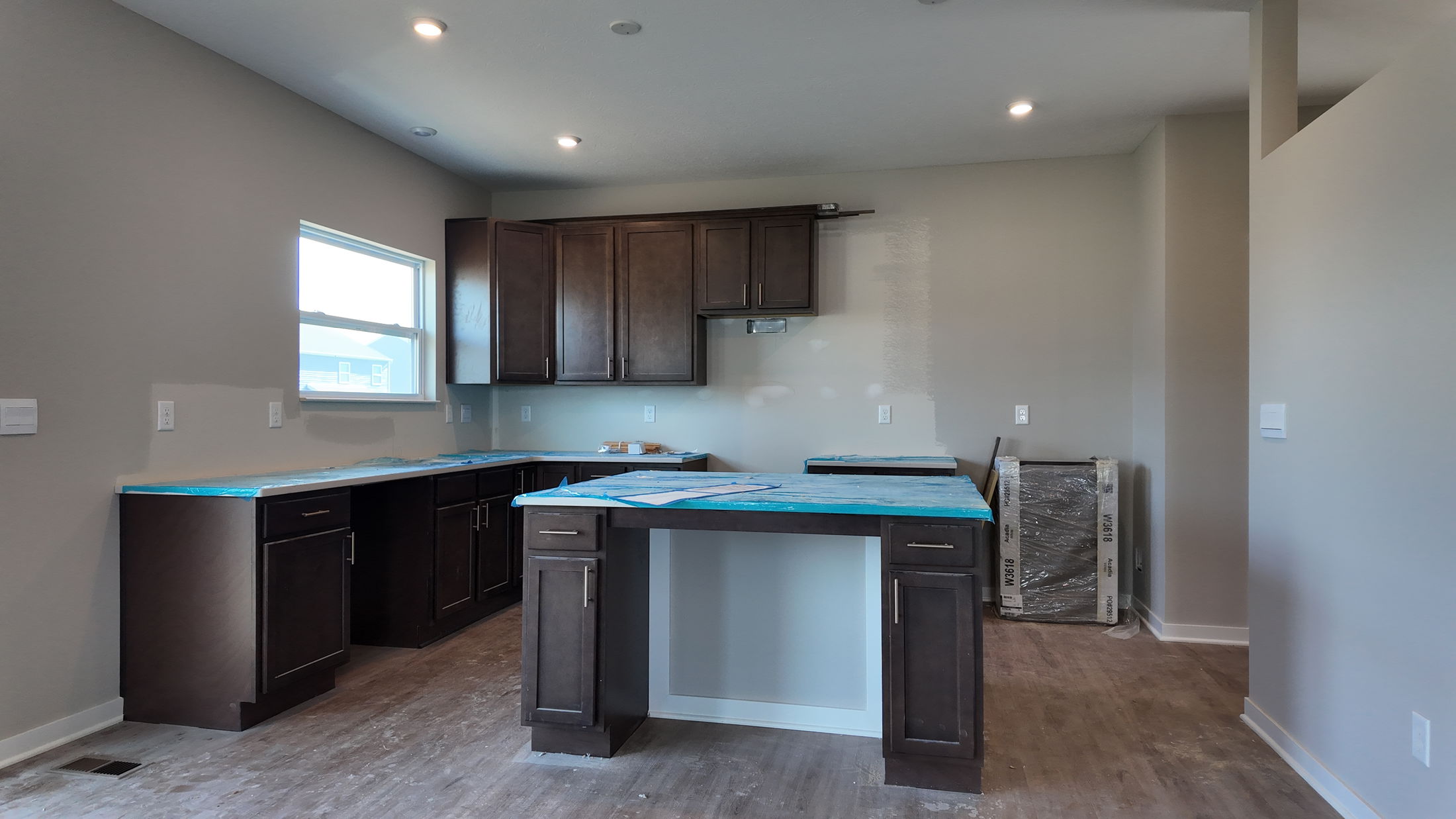 Modern kitchen under construction featuring dark wood cabinets, a kitchen island, and partially installed countertops.