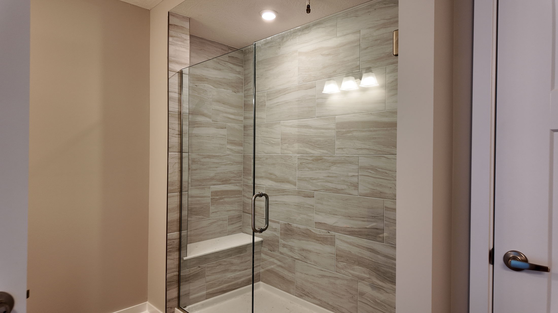 Modern bathroom with a glass-enclosed walk-in shower featuring stylish beige wall tiles.