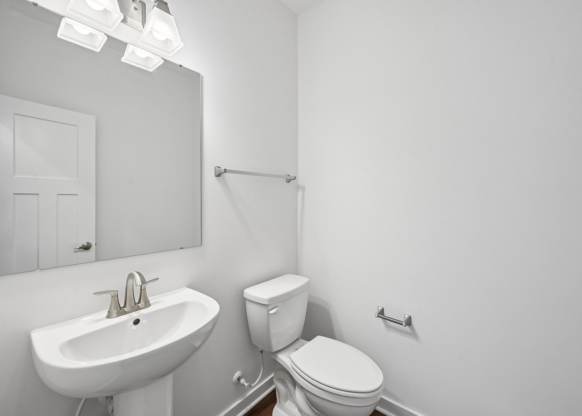 Bright, modern bathroom featuring a sink, toilet, and large mirror against white walls.