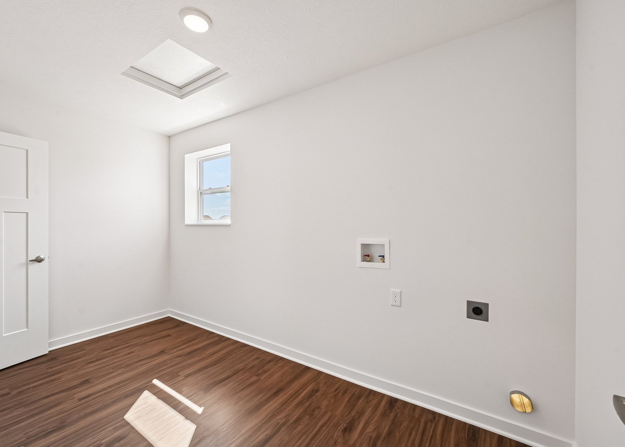 Empty interior room with white walls, a window, and wood-like flooring.