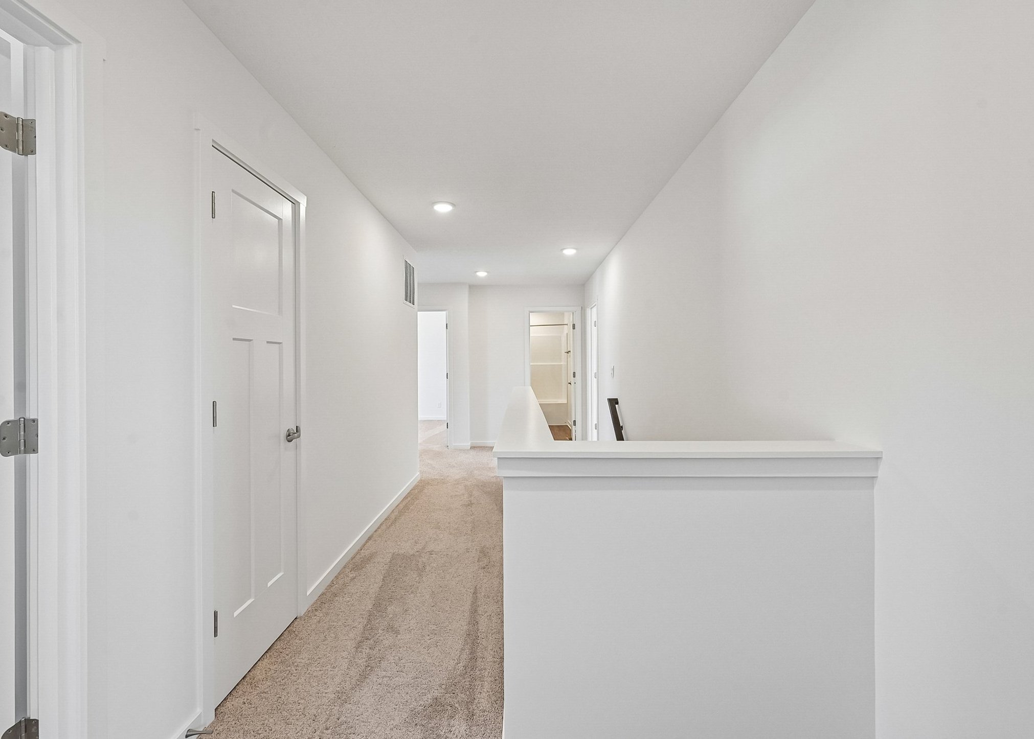 A well-lit hallway with white walls and carpet leading to open doorways.