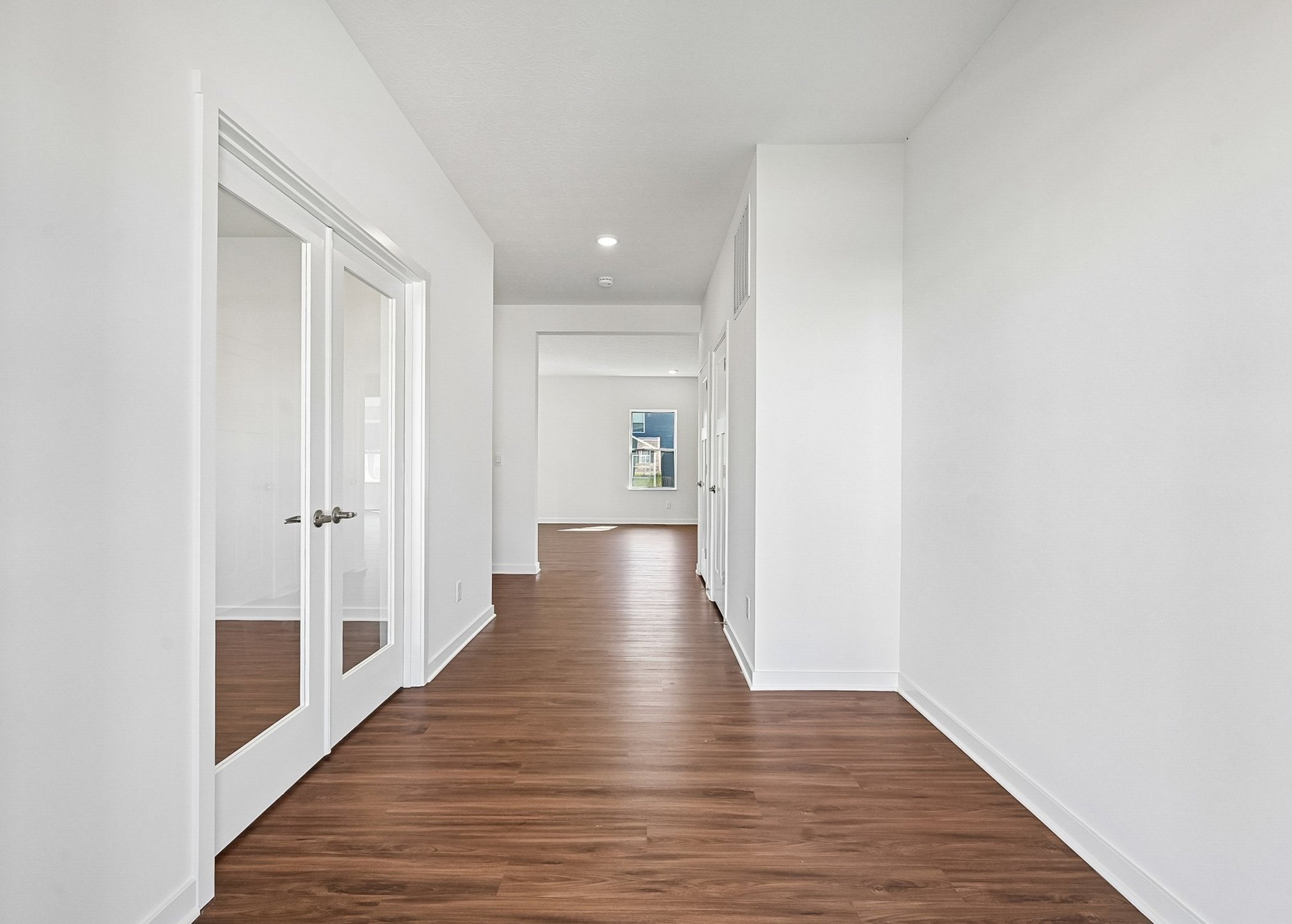 Bright hallway with wood flooring and glass-paned doors leading to adjoining rooms.