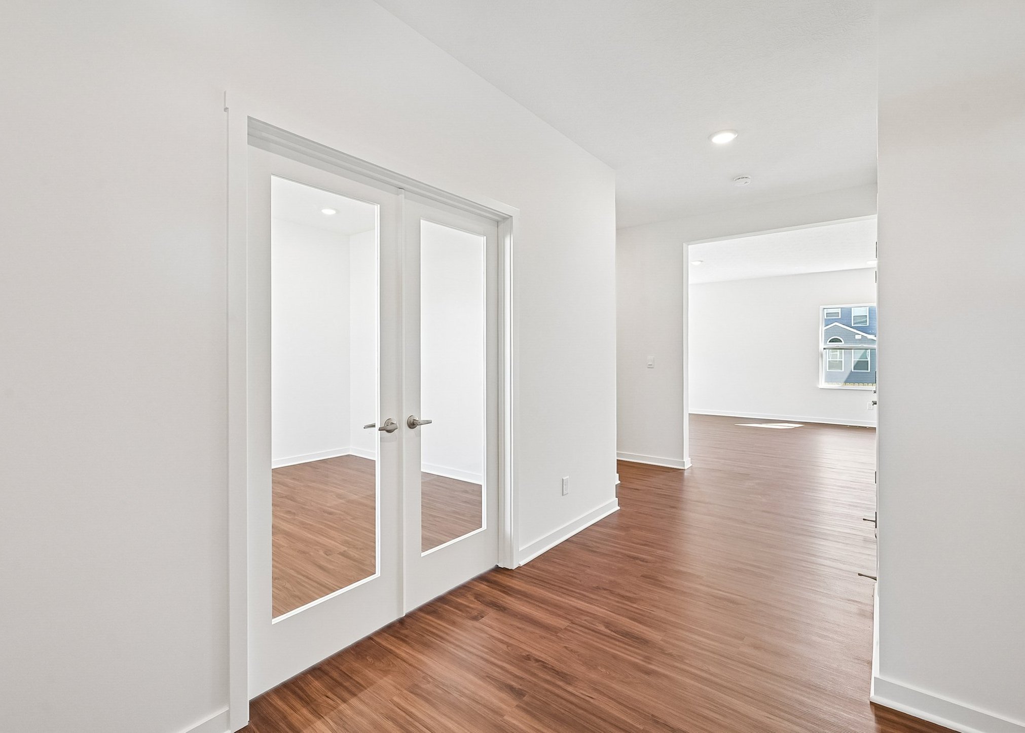 Bright interior space featuring hardwood floors and double glass doors leading to another room.